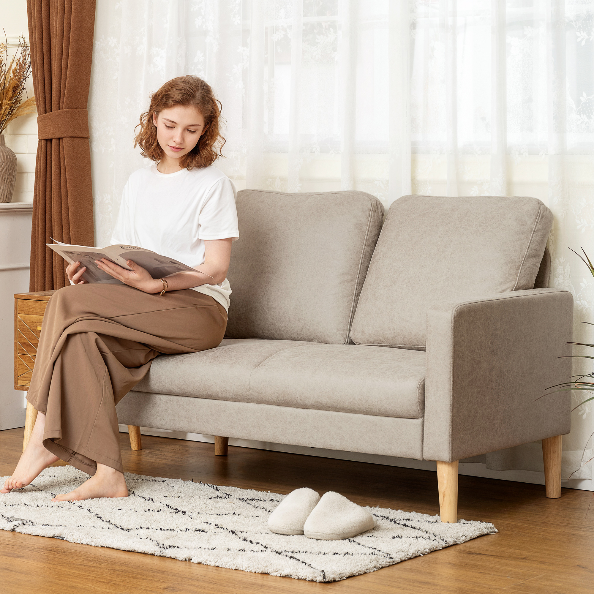 Una mujer se sienta en un sofá beige leyendo una revista. Tiene las piernas cruzadas.