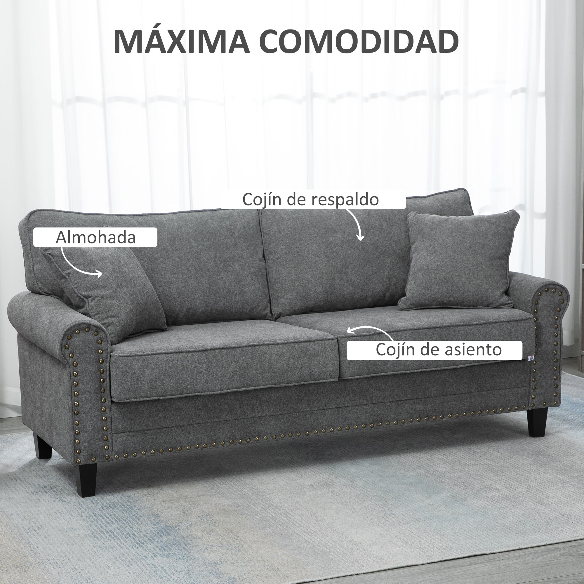 Un sofá gris con tachuelas decorativas y cojines mullidos sobre una alfombra estampada.