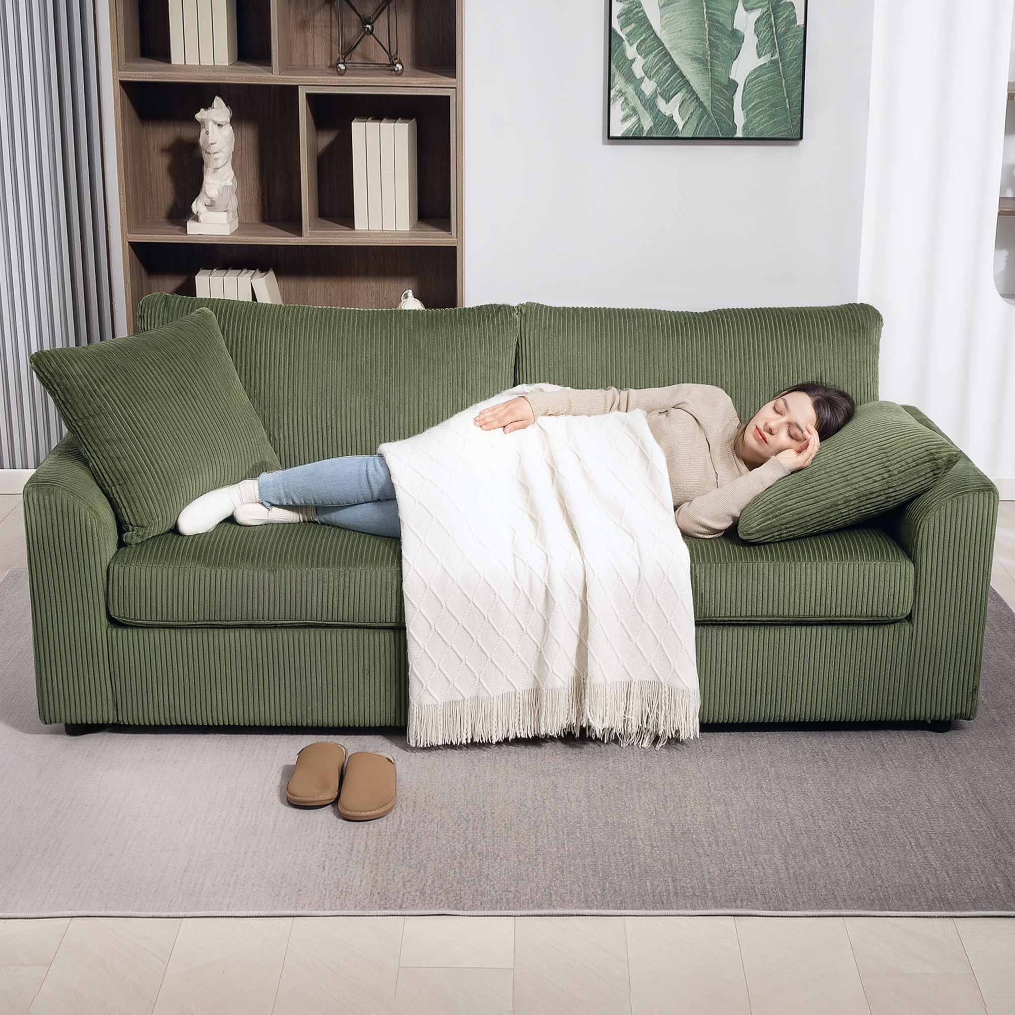 Una mujer duerme en un sofá verde, cubierta con una manta blanca.