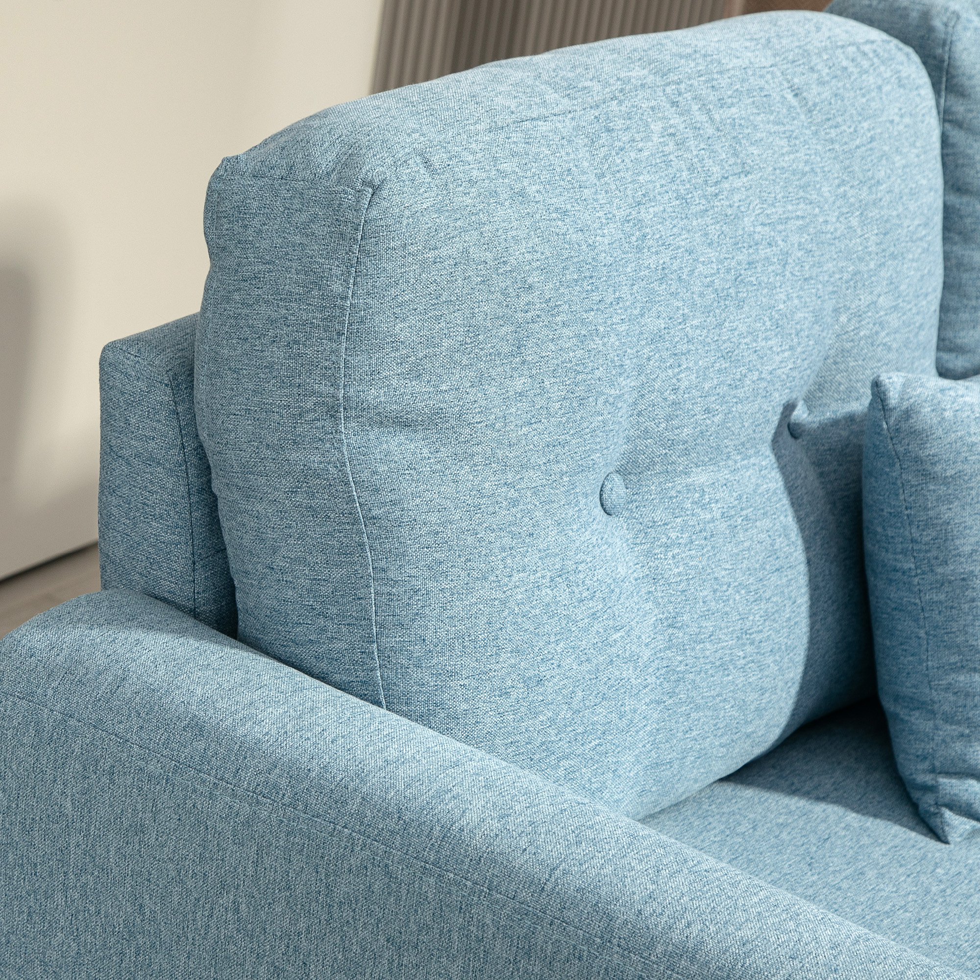 Un sofá azul claro con capitoné y costuras visibles. Una almohada pequeña está a la derecha.