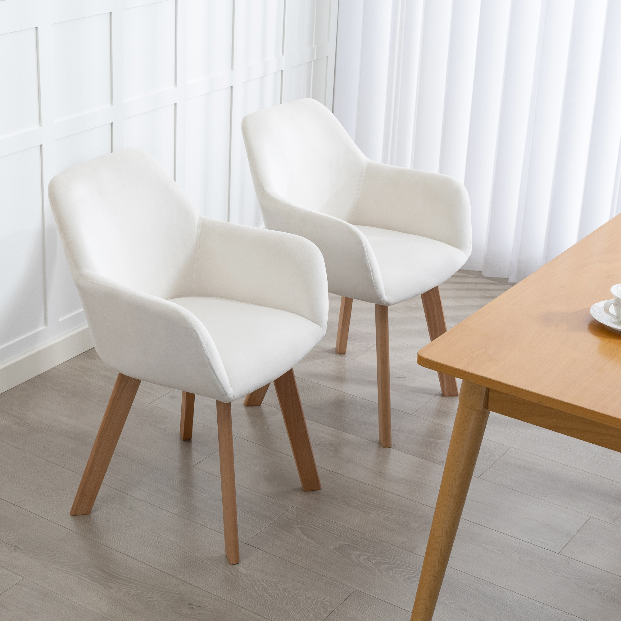 Dos sillones blancos están junto a una mesa de madera sobre suelo de madera gris.
