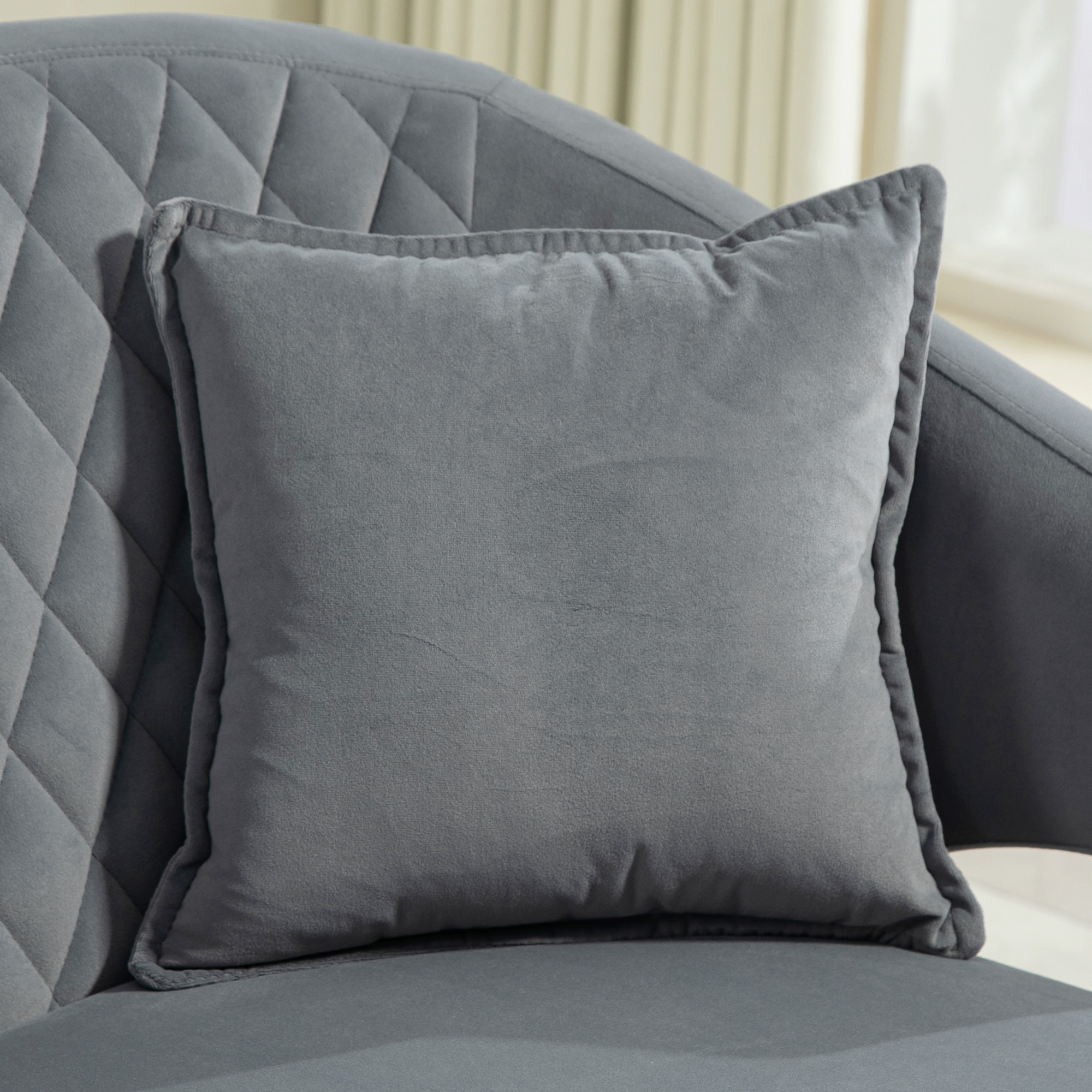 Un cojín gris descansa sobre un sillón gris con patrón de diamantes.