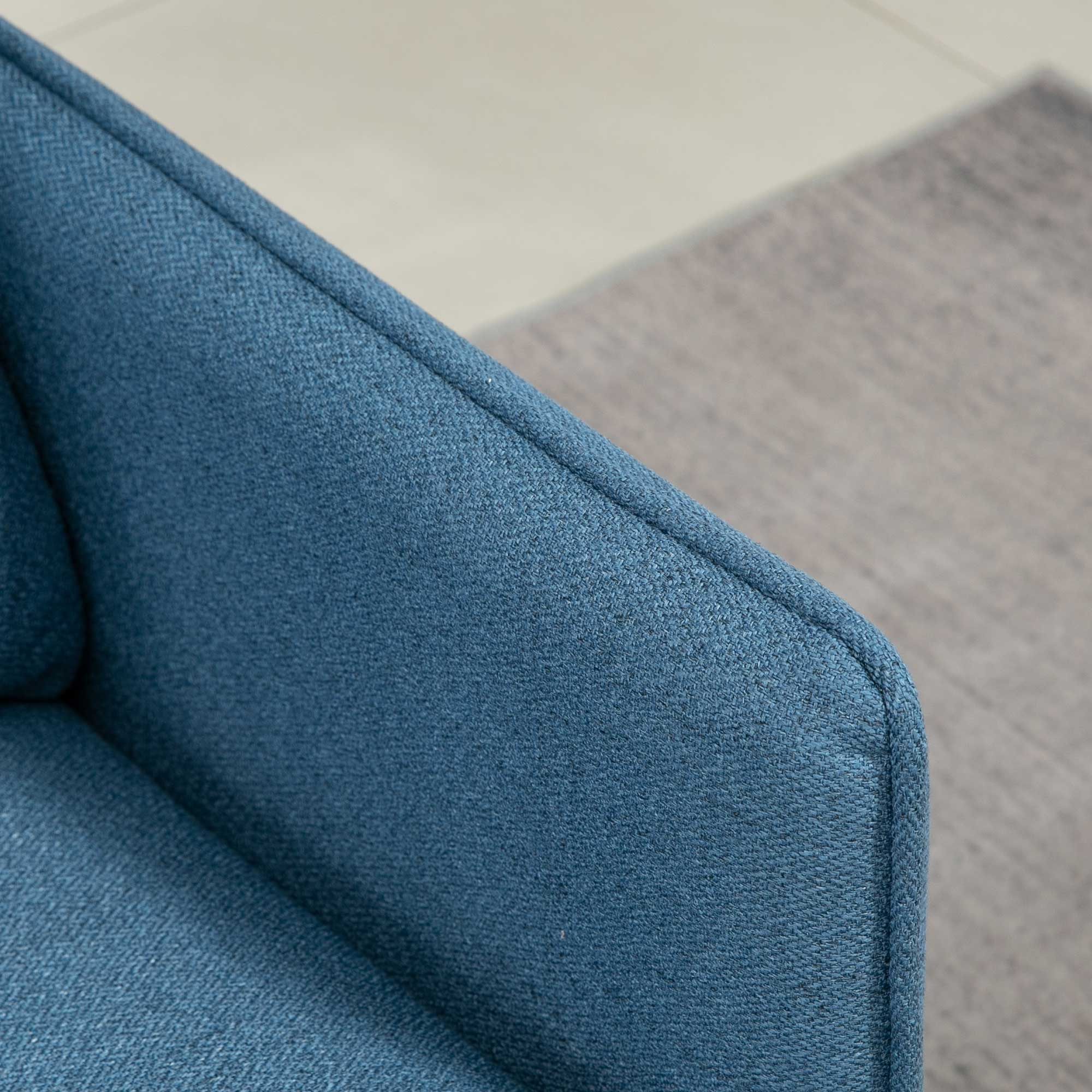 Primer plano de una silla de tela azul con alfombra y baldosas de fondo.