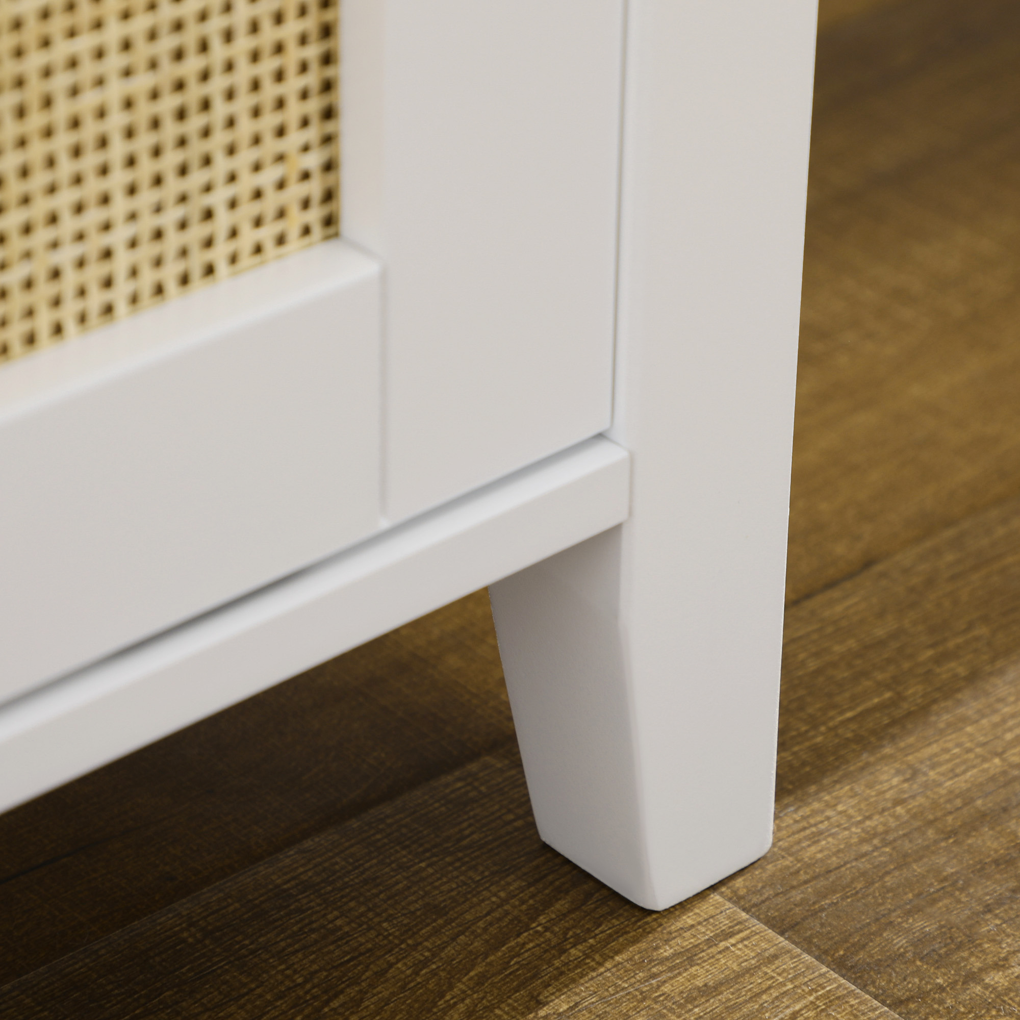 Primer plano de pata de mueble blanca sobre suelo de madera, con tejido de ratán detrás.