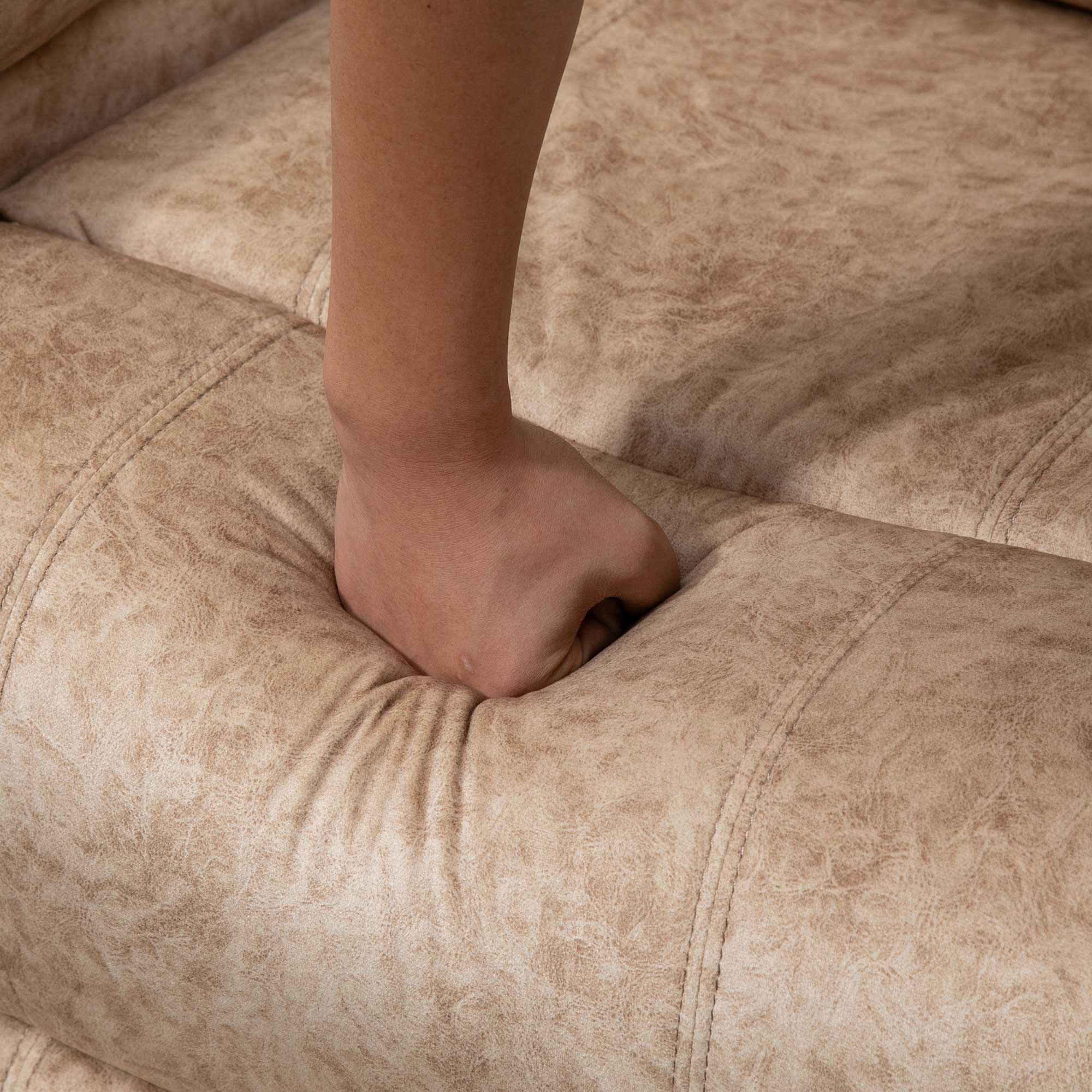 Una mano presiona la superficie acolchada beige de un sofá.