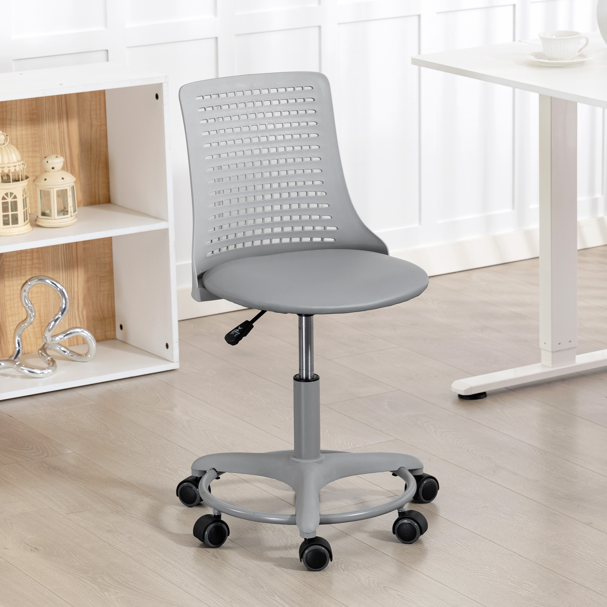 Una silla de oficina gris con ruedas se encuentra frente a una mesa y estante blancos.