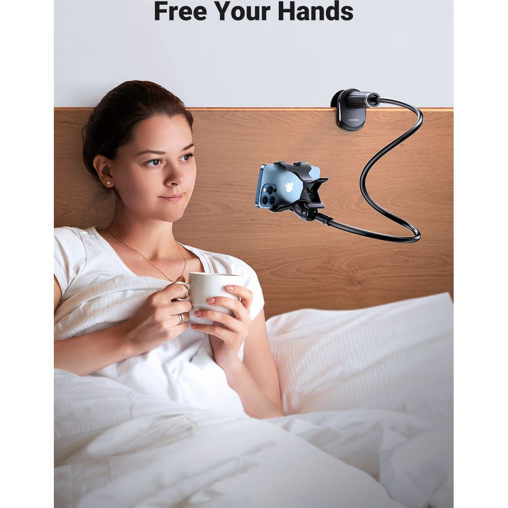 Kobieta pije kawę w łóżku z uchwytem na telefon przy zagłówku.