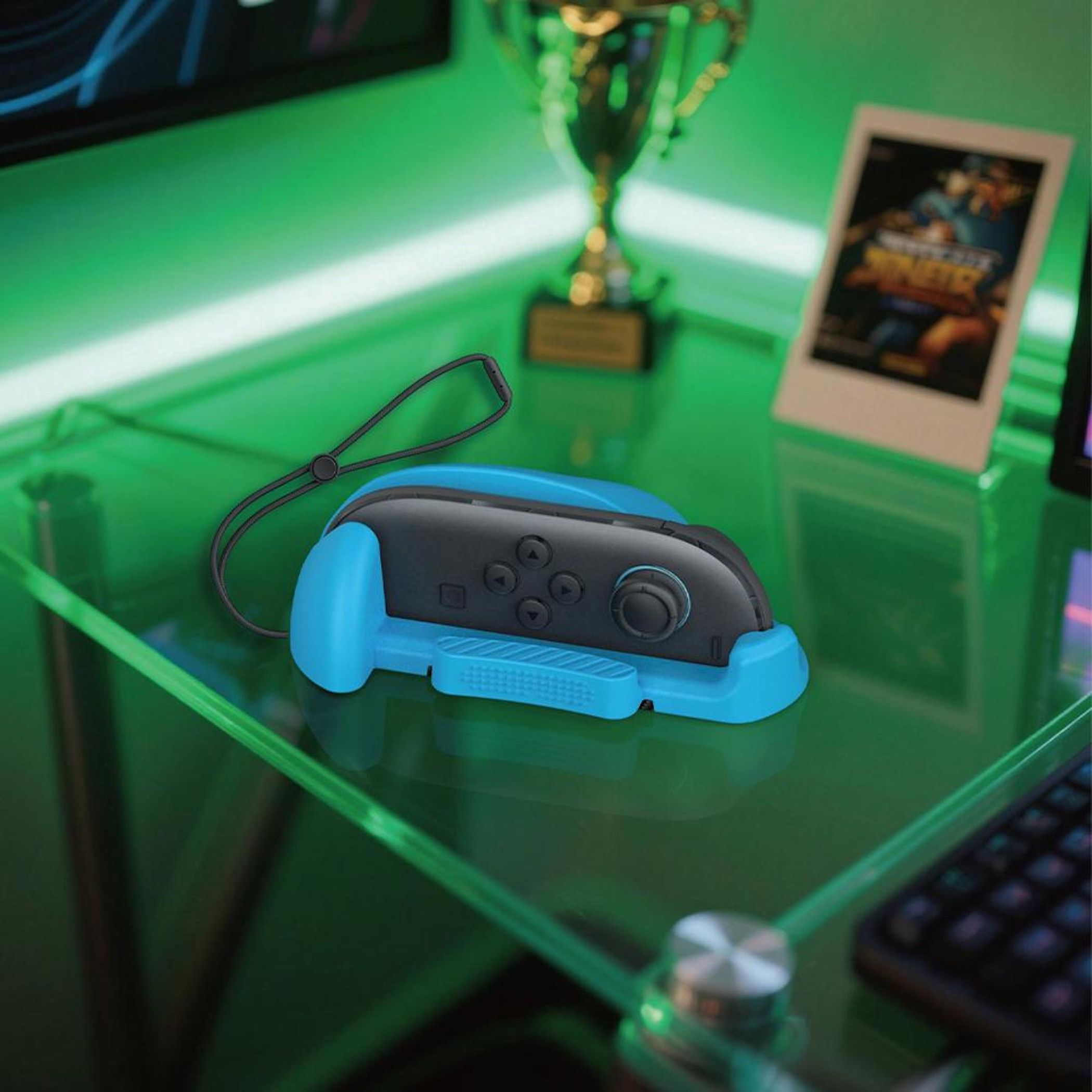 Blaue Controller-Halterung mit Trageband auf grünem Glastisch, Trophäe und Foto.