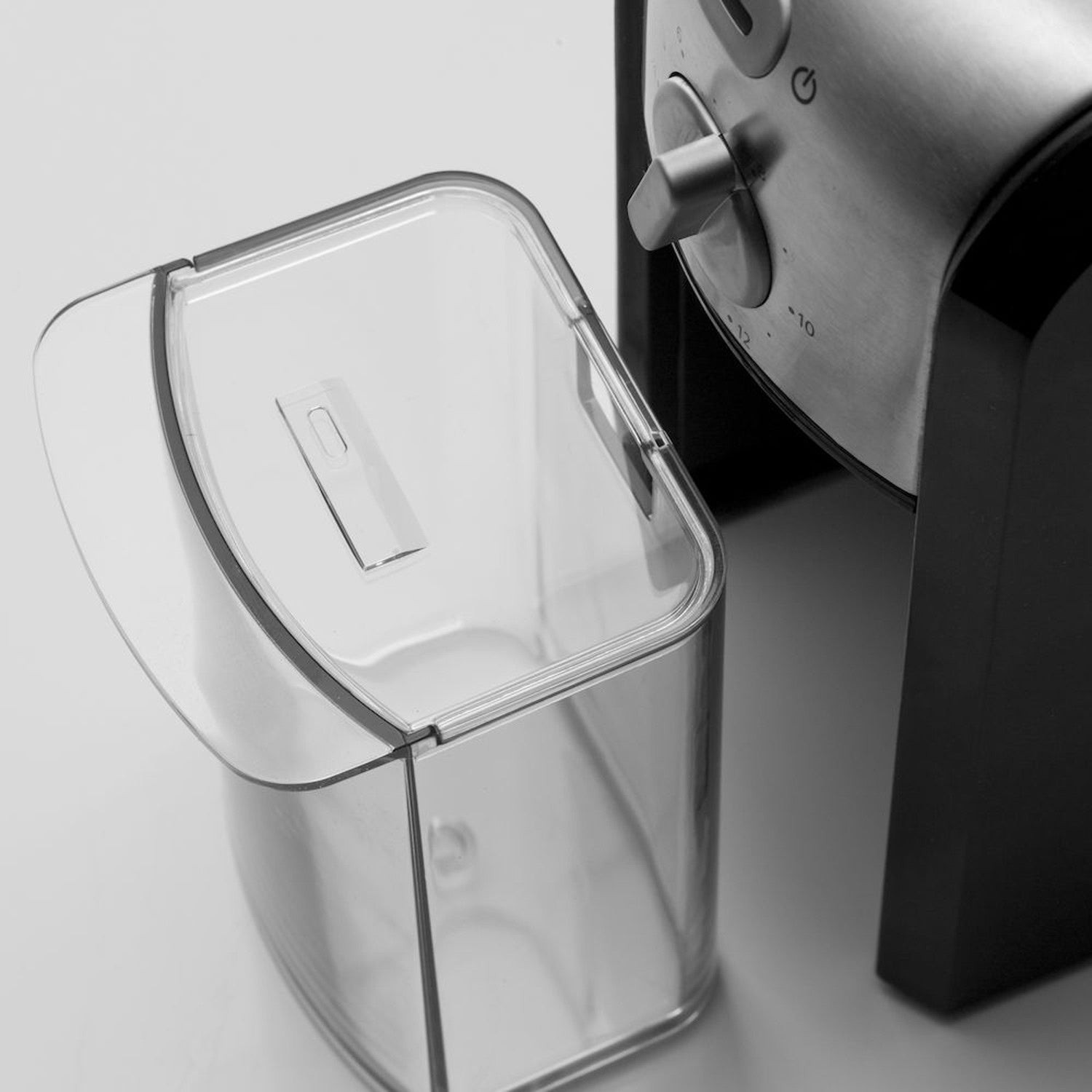 A clear container next to a coffee grinder body with a dial.