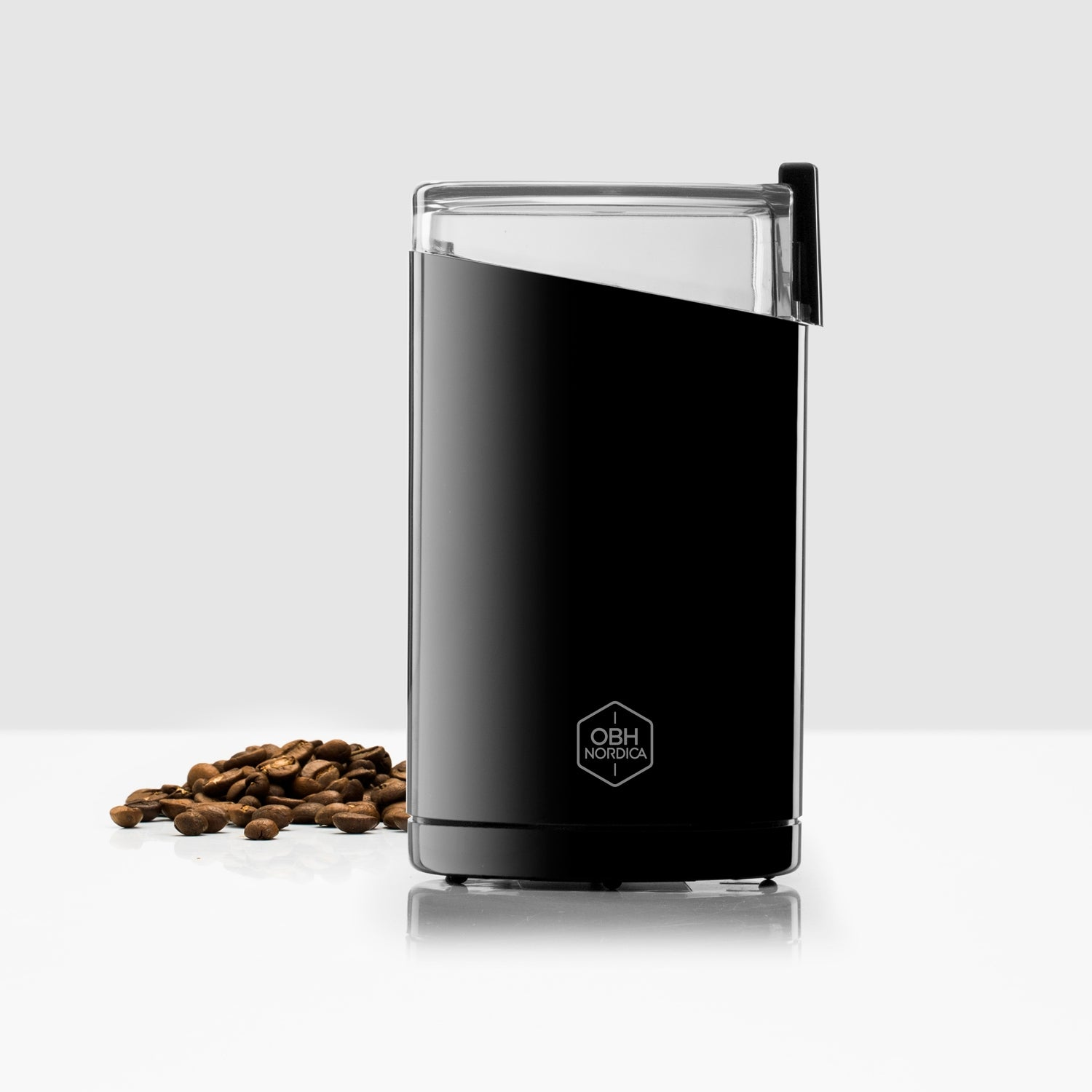 Black coffee grinder with clear lid and coffee beans beside it.