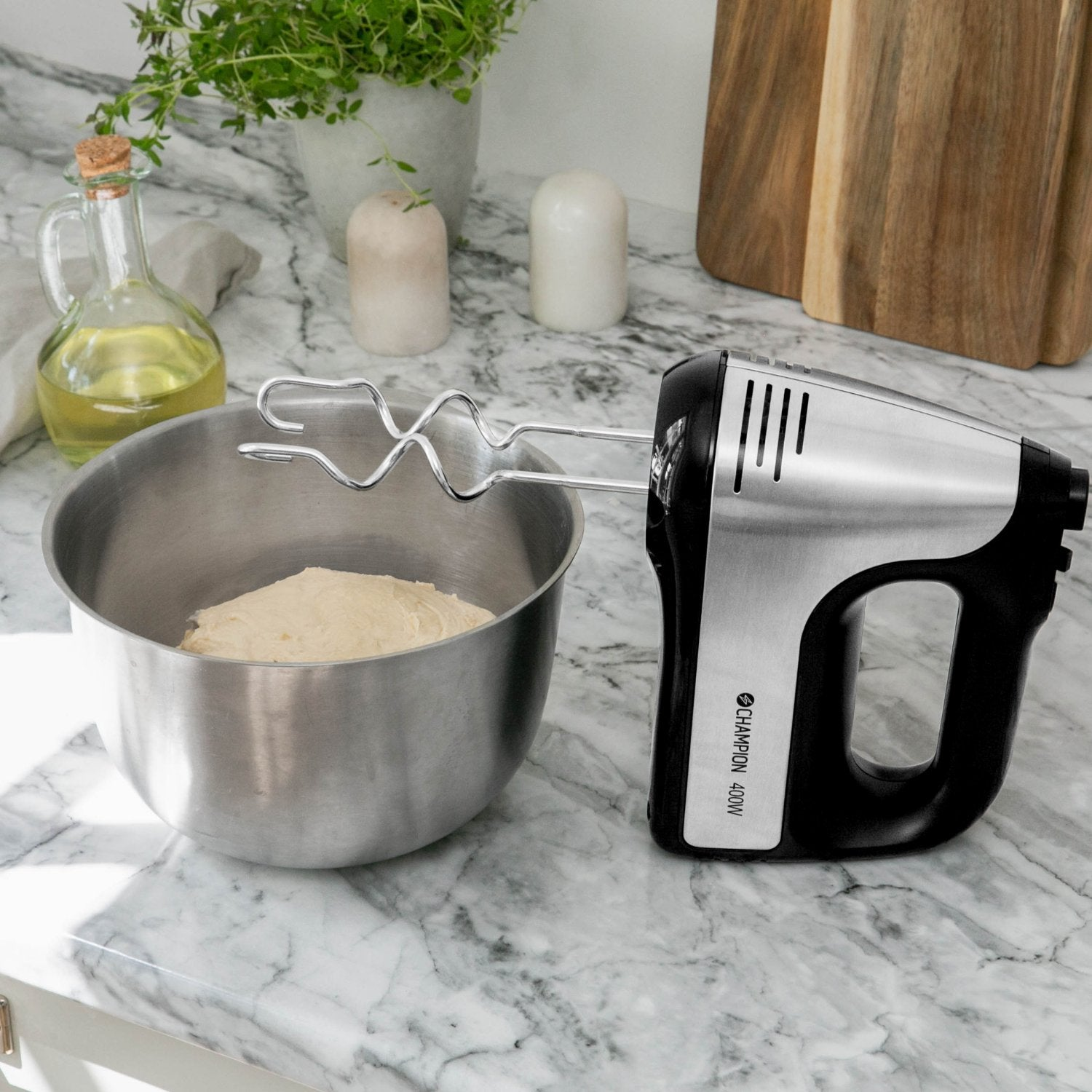 A silver and black hand mixer sits beside a stainless steel bowl with dough.