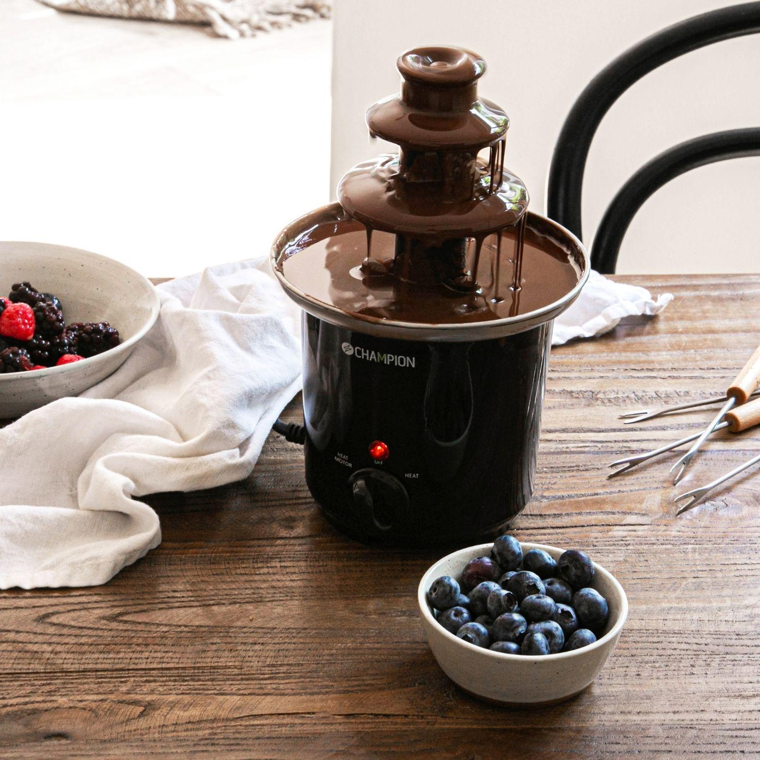 Een chocoladefontein stroomt met chocolade naast kommen met bessen en blauwe bessen.