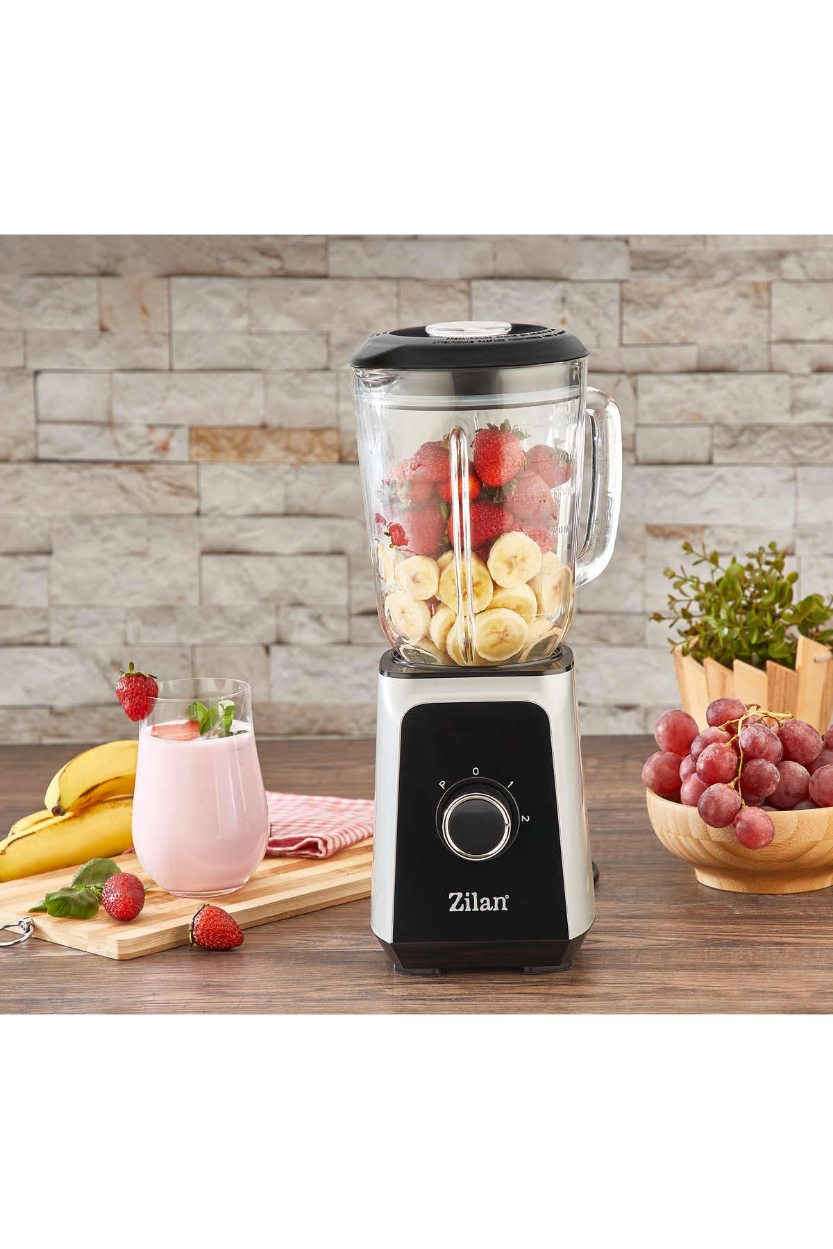 Çilek ve muzlu blender, yanında bir bardak smoothie ve üzüm var.