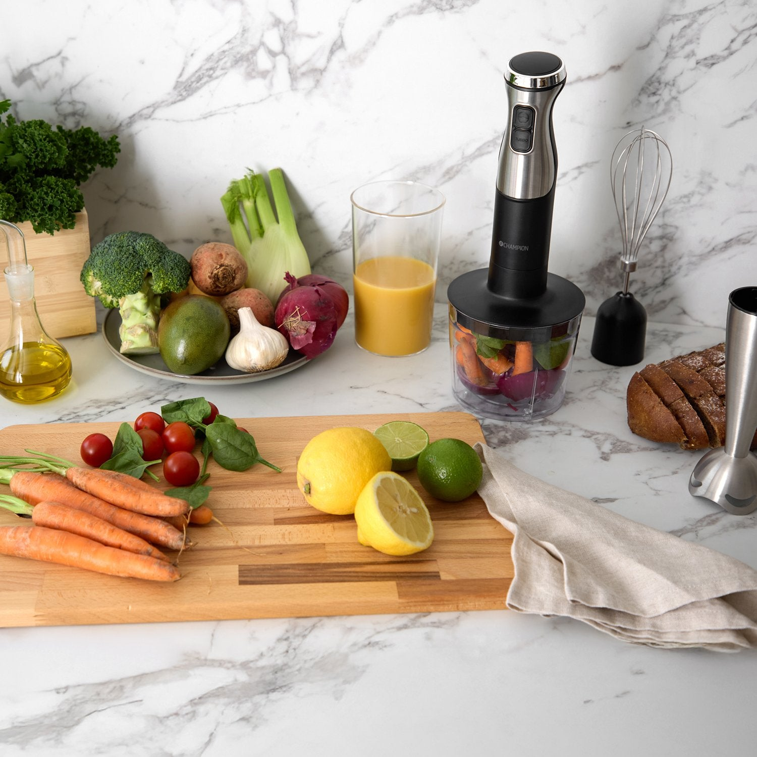 An immersion blender with accessories and fresh vegetables on a marble countertop.