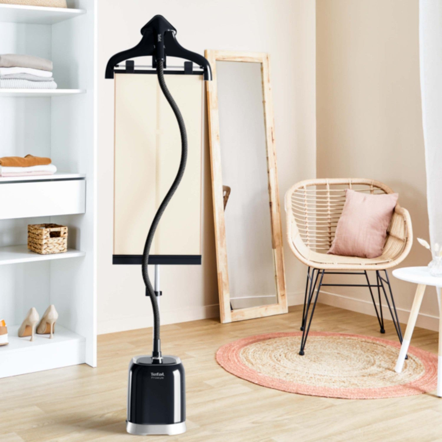 A garment steamer stands next to a mirror and a wicker chair with a pillow.