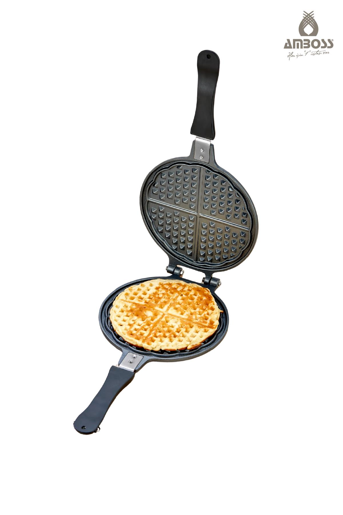 Beyaz zeminde açık, siyah bir waffle makinesinde yuvarlak, altın rengi waffle.