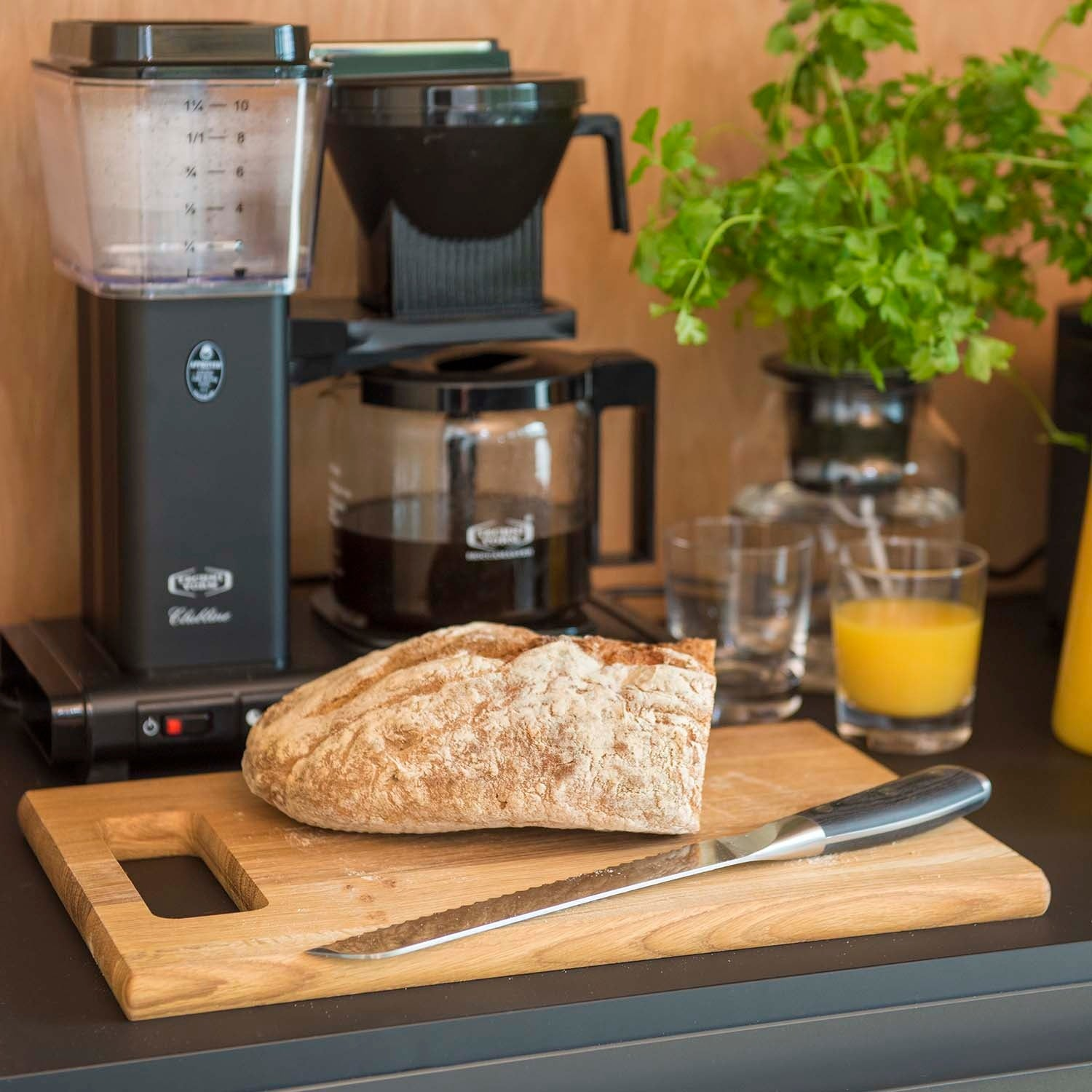 Koffiezetapparaat met kan, brood, mes, sap en groene planten.