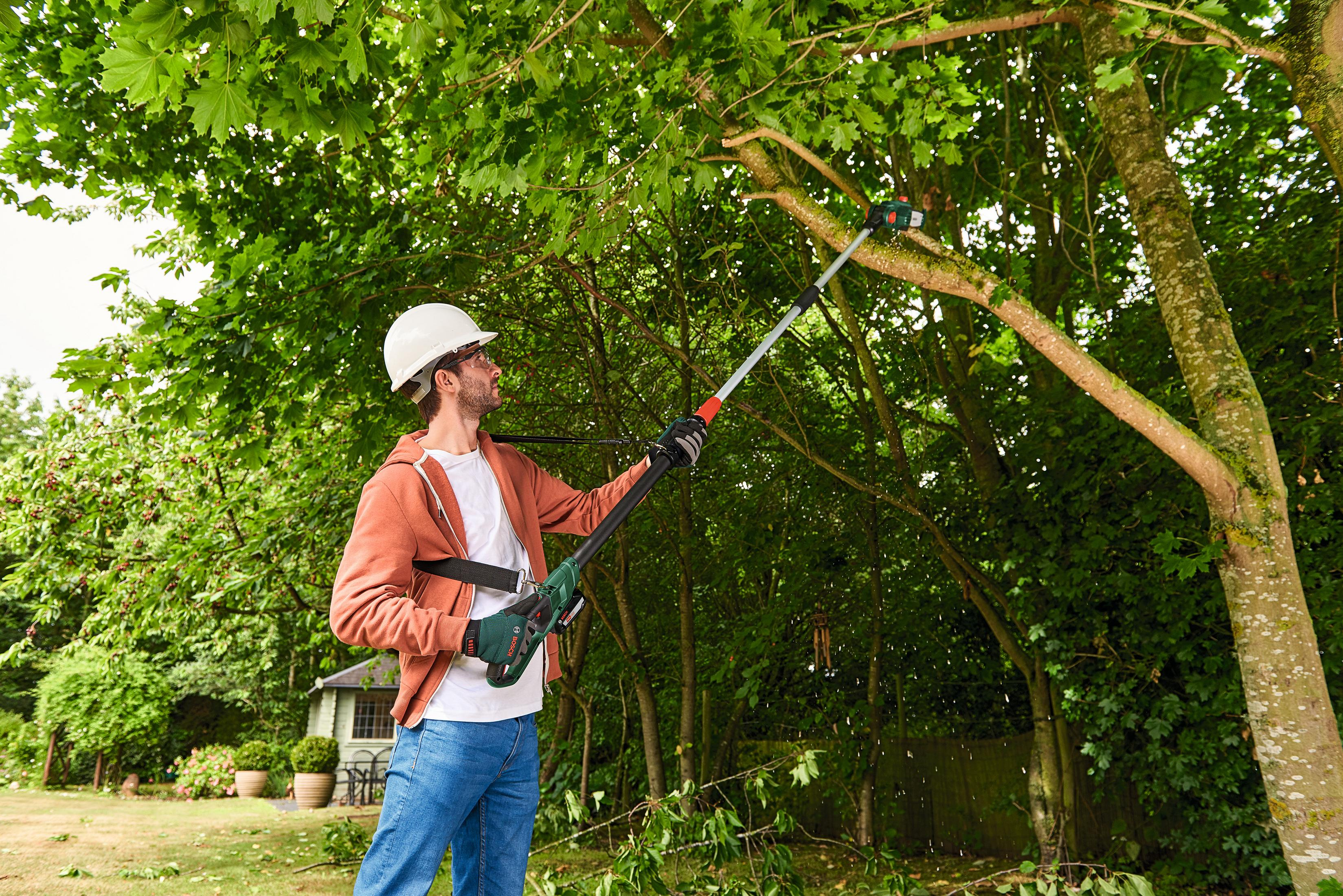 Mann in weiem Helm schneidet Ast mit Astschere in einem Garten.
