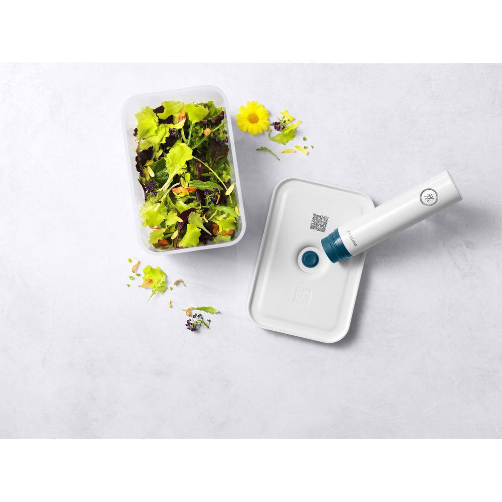 Un contenitore di insalata accanto a un sottovuoto con manico bianco su coperchio bianco.