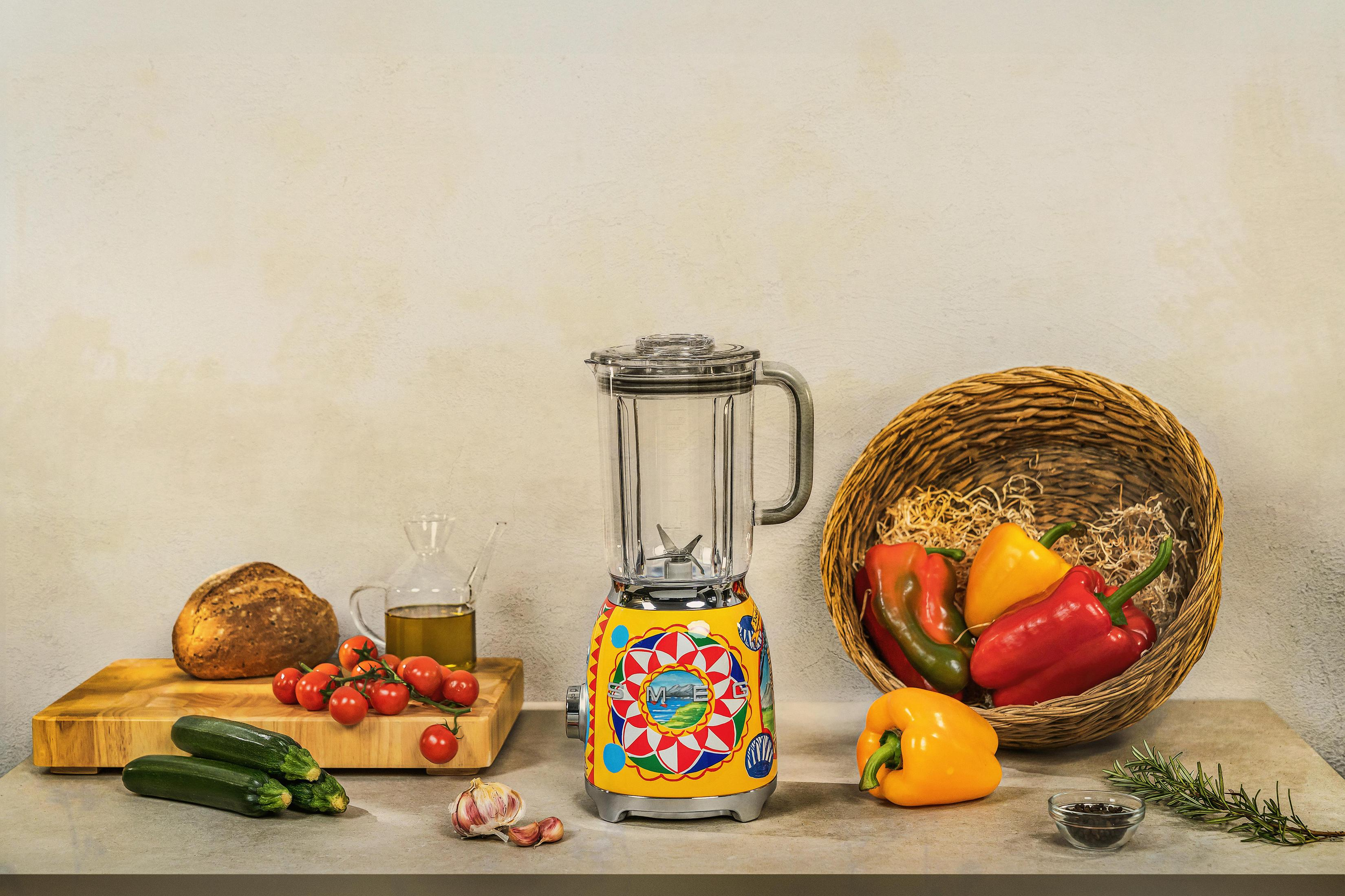 Licuadora colorida con verduras, pan y aceite en una encimera.