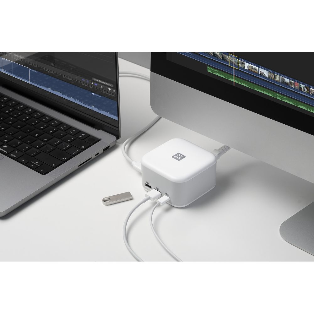 Een witte USB-hub staat tussen een laptop en een monitor op een bureau.
