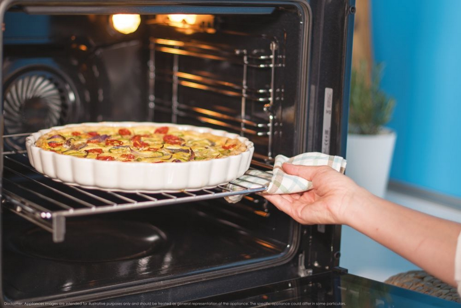 Una mano con un panno estrae una quiche da un forno aperto.
