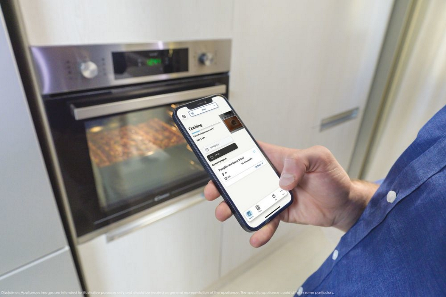 Una mano tiene uno smartphone che mostra i controlli del forno accanto a un forno moderno con cibo all'interno.