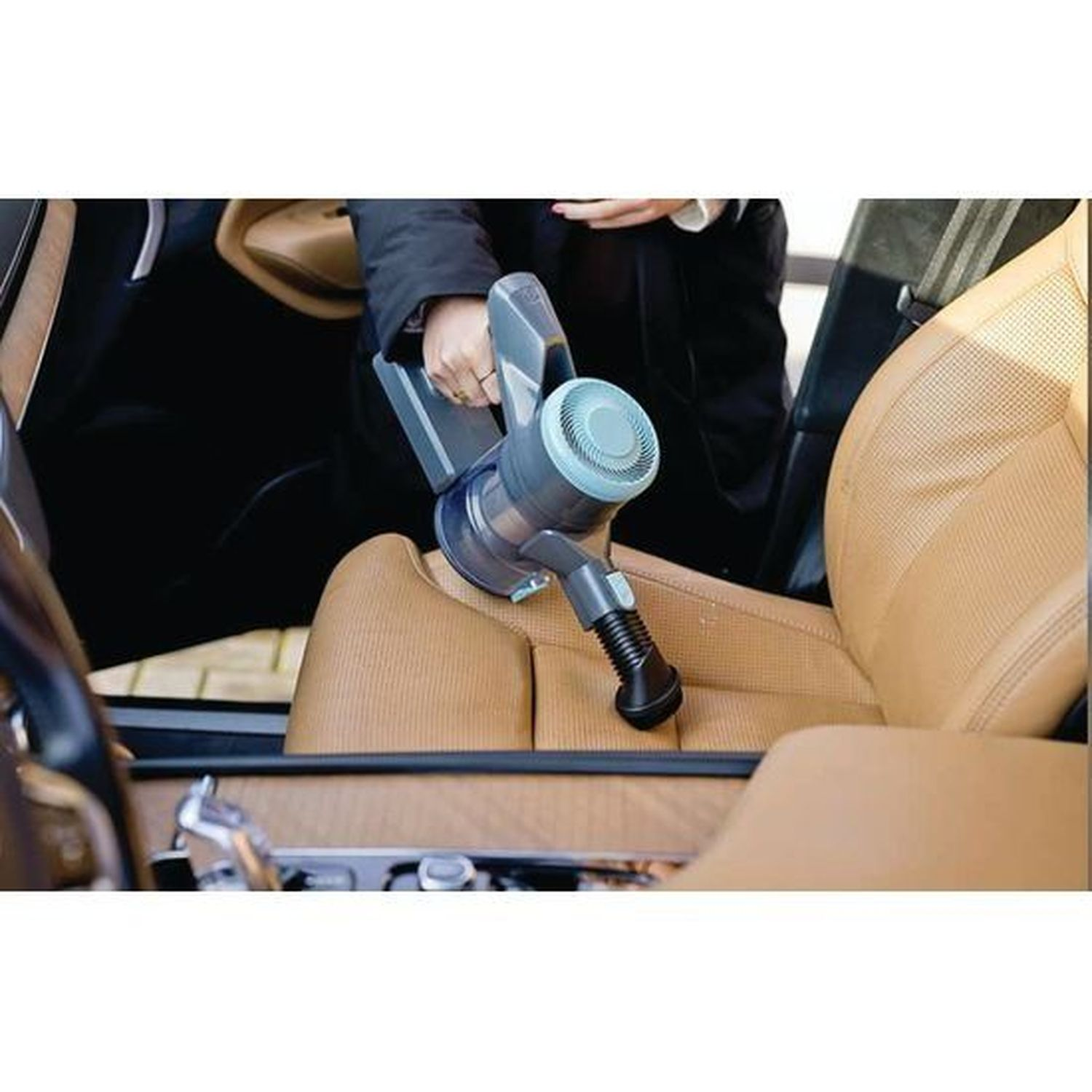 Person cleaning brown leather car seats with a handheld vacuum cleaner.