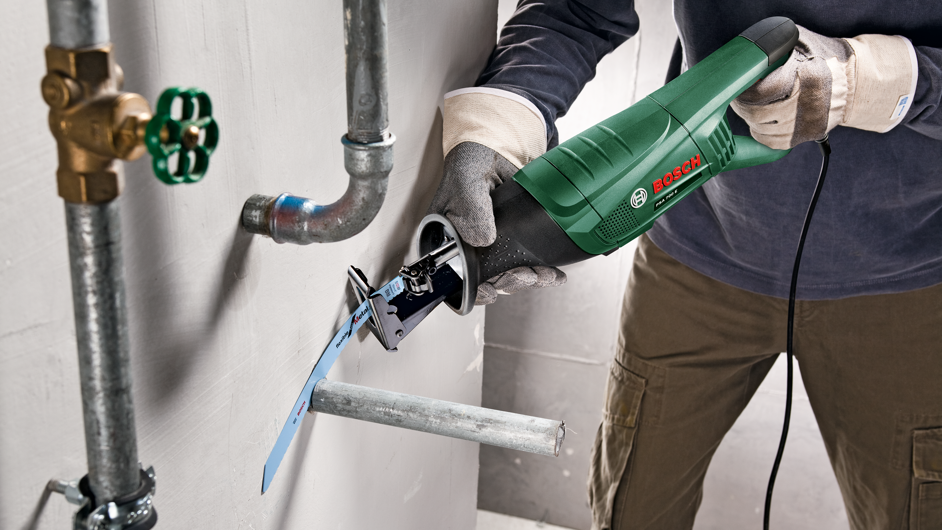 Zielona wyrzynarka Bosch tnie metalową rurę obok kranu i rurociągu.