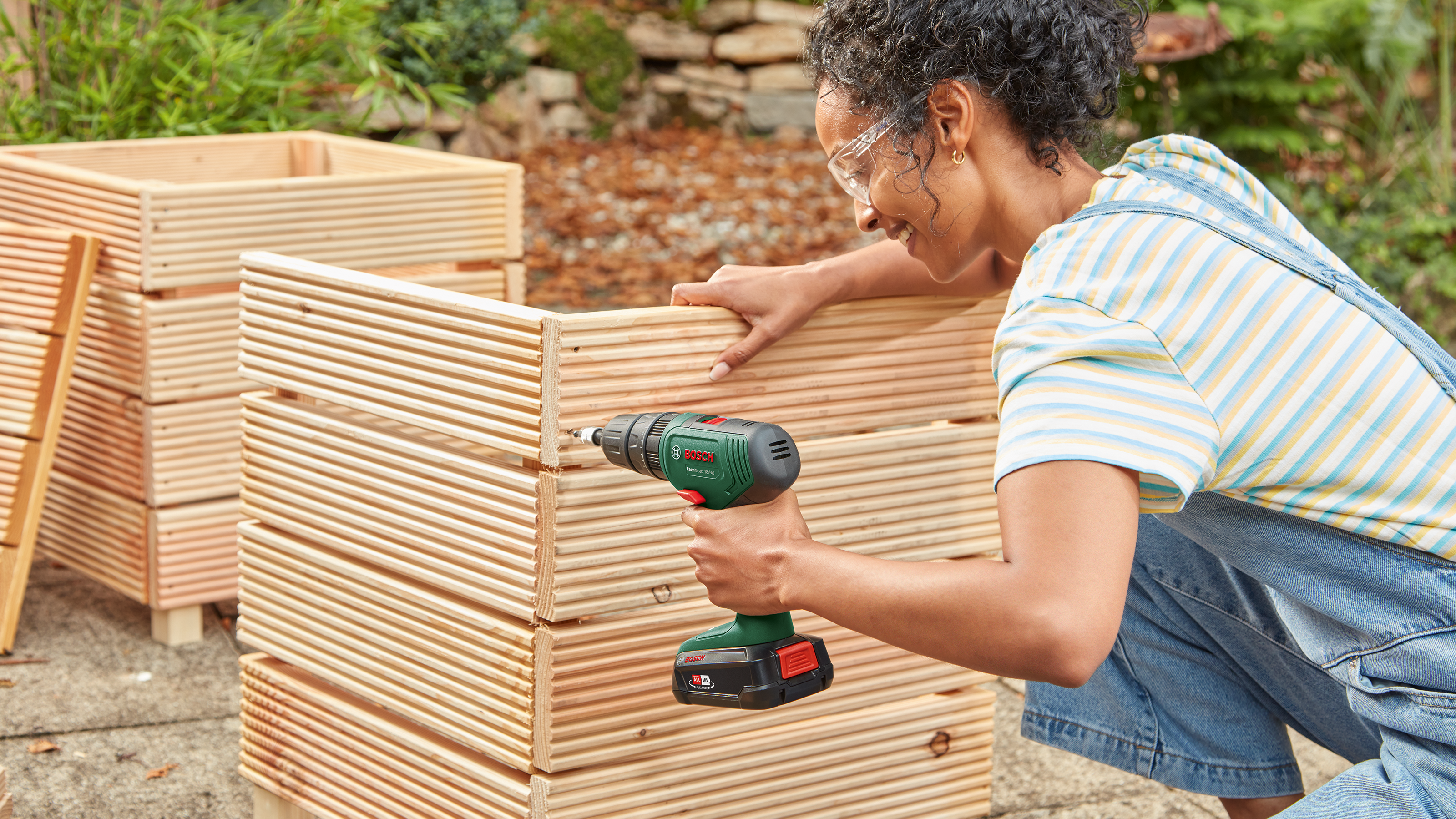 Frau baut Holzkasten mit Bohrmaschine im Garten.