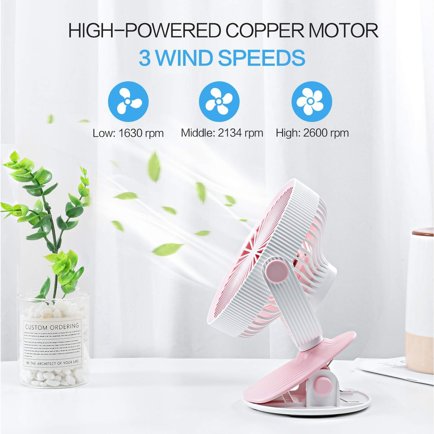 Ein kleiner rosa und weißer Ventilator mit drei Geschwindigkeiten, auf einem Schreibtisch.