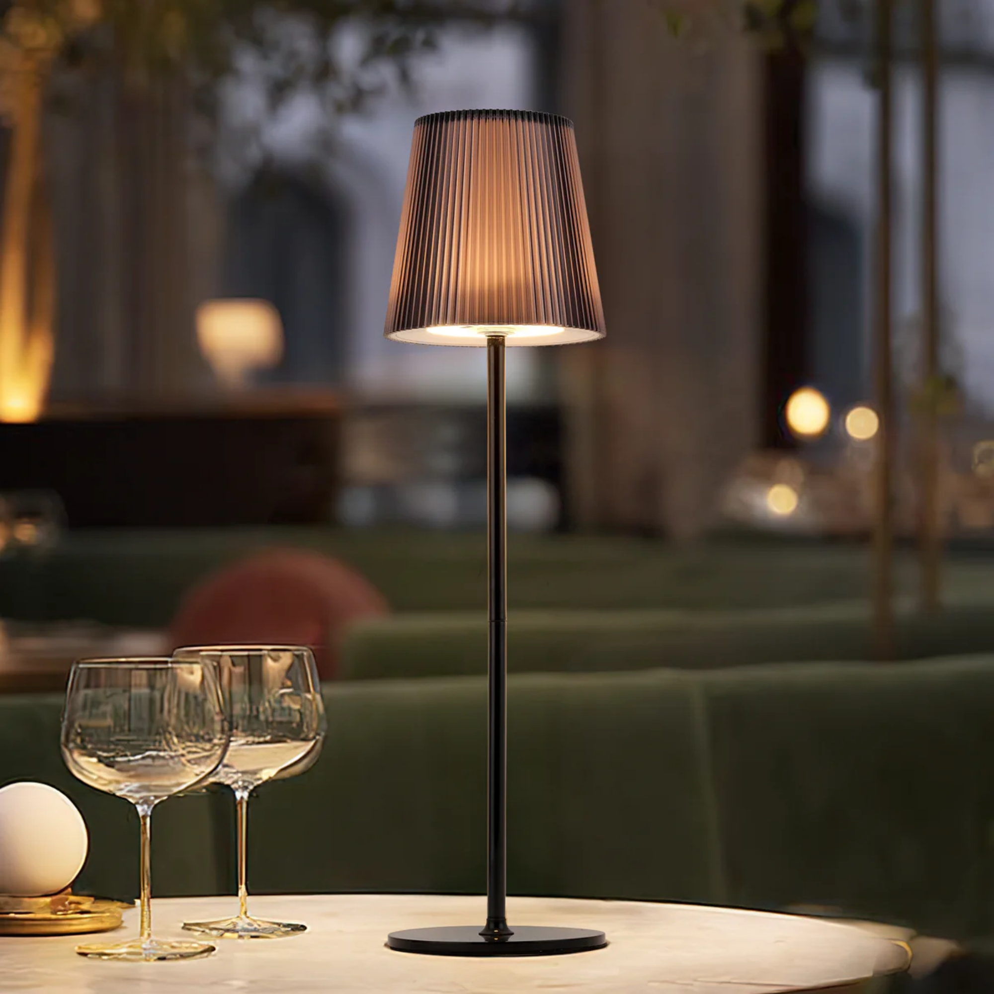 Eine Lampe mit geripptem Schirm steht auf einem Tisch mit zwei Weingläsern.