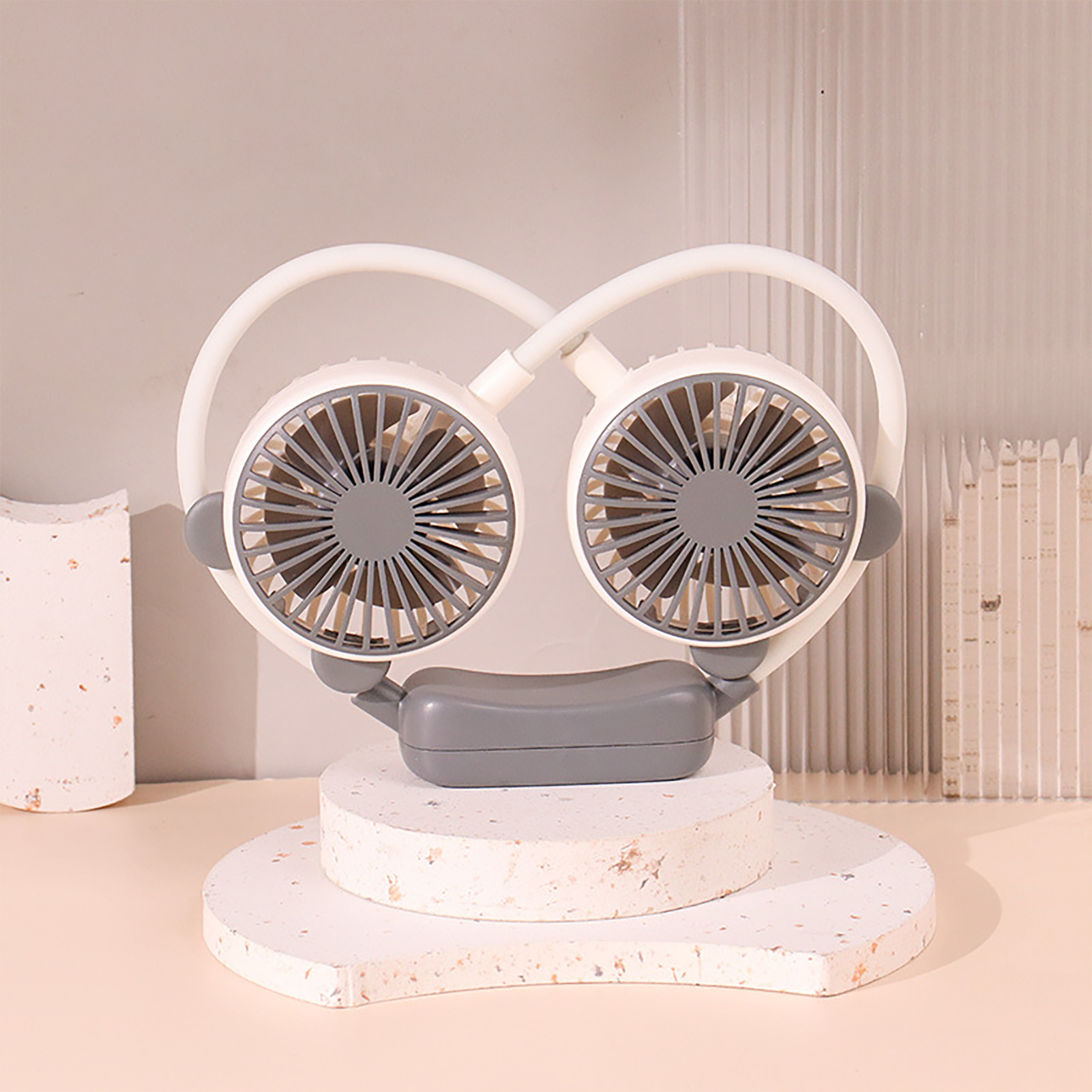 Ein tragbarer Nackenventilator mit zwei Lüftern, weiß und grau, auf Podesten.