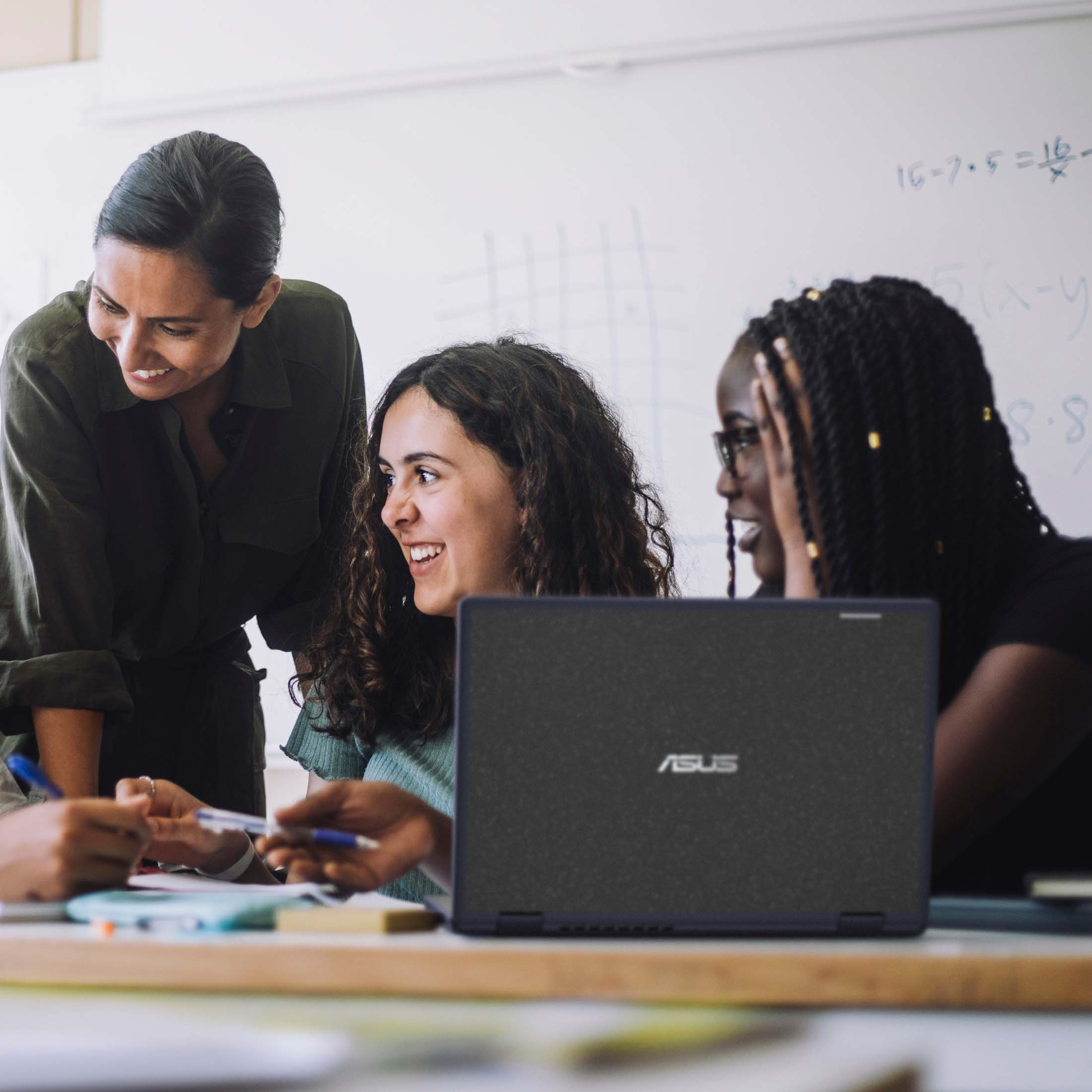 Drei Frauen lachen und lernen an einem Tisch mit einem Laptop.