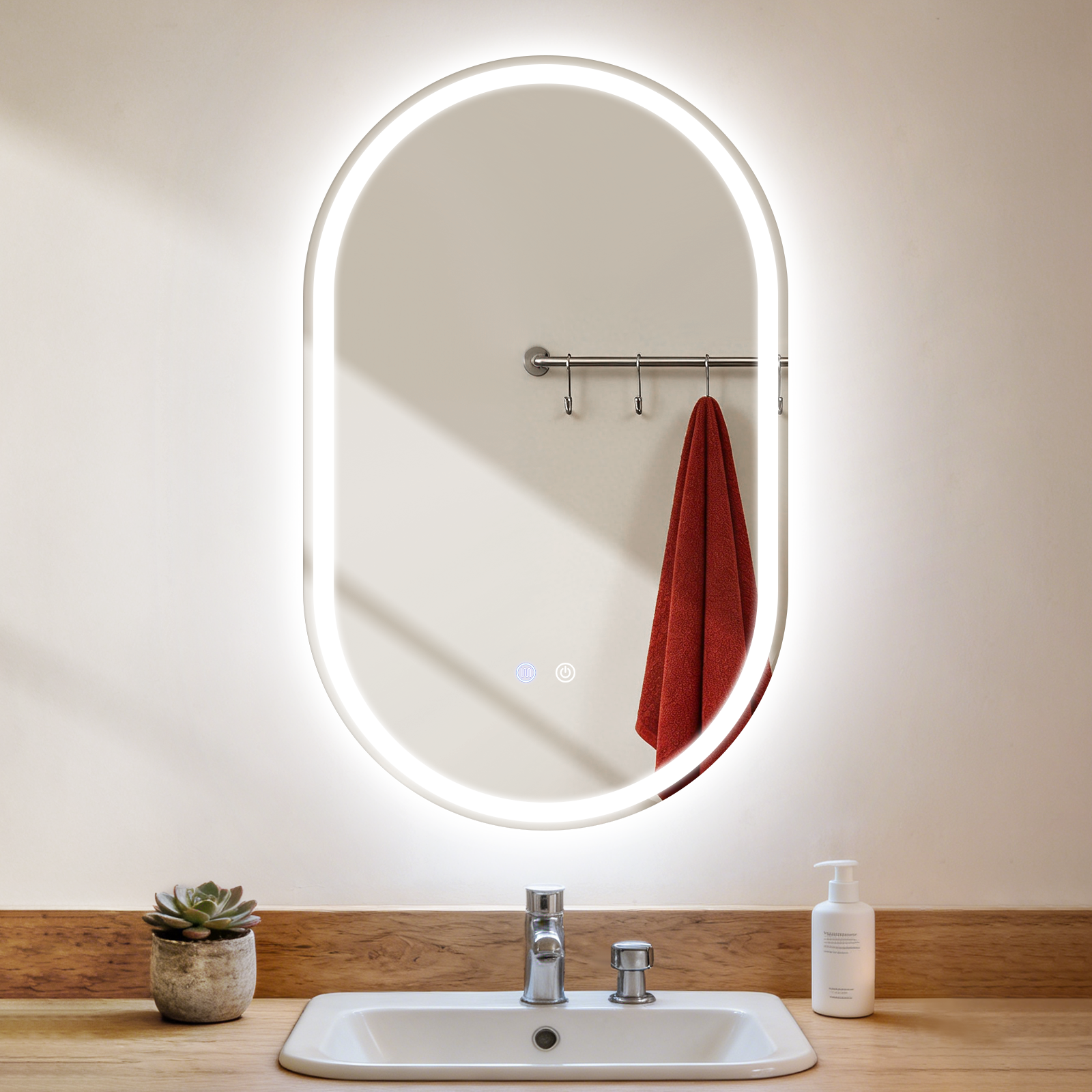 Un espejo ovalado iluminado sobre un lavabo con grifos, jabón y planta.