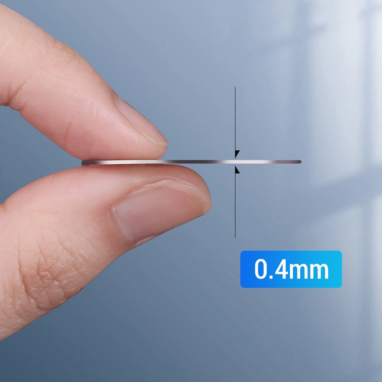 Kciuk i palec wskazujący trzymają cienki, srebrny dysk z napisem 0,4 mm.