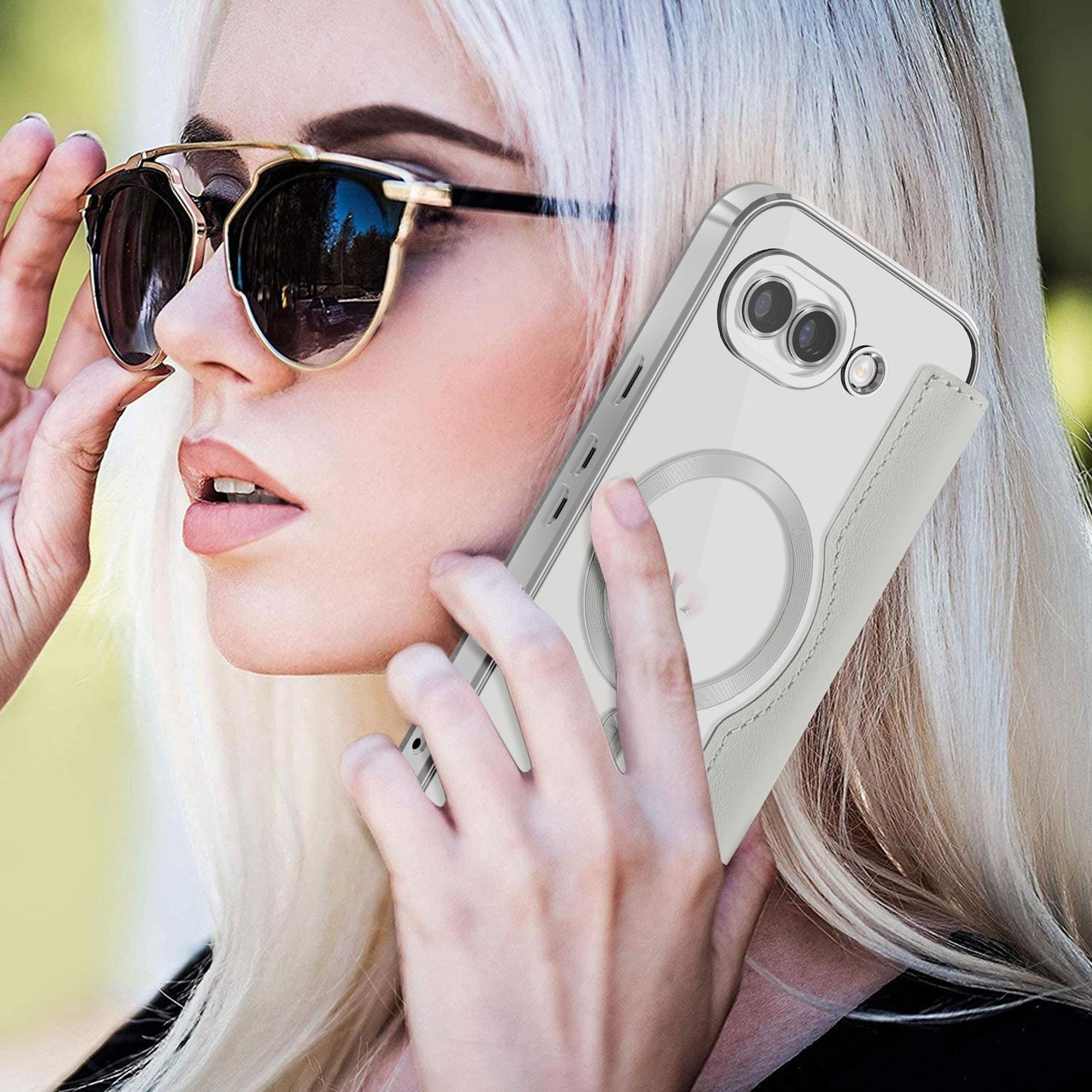 Eine hellhäutige Frau mit blonden Haaren und Sonnenbrille hält ein Telefon mit einer durchsichtigen Hülle und weißem Riemen ans Ohr.