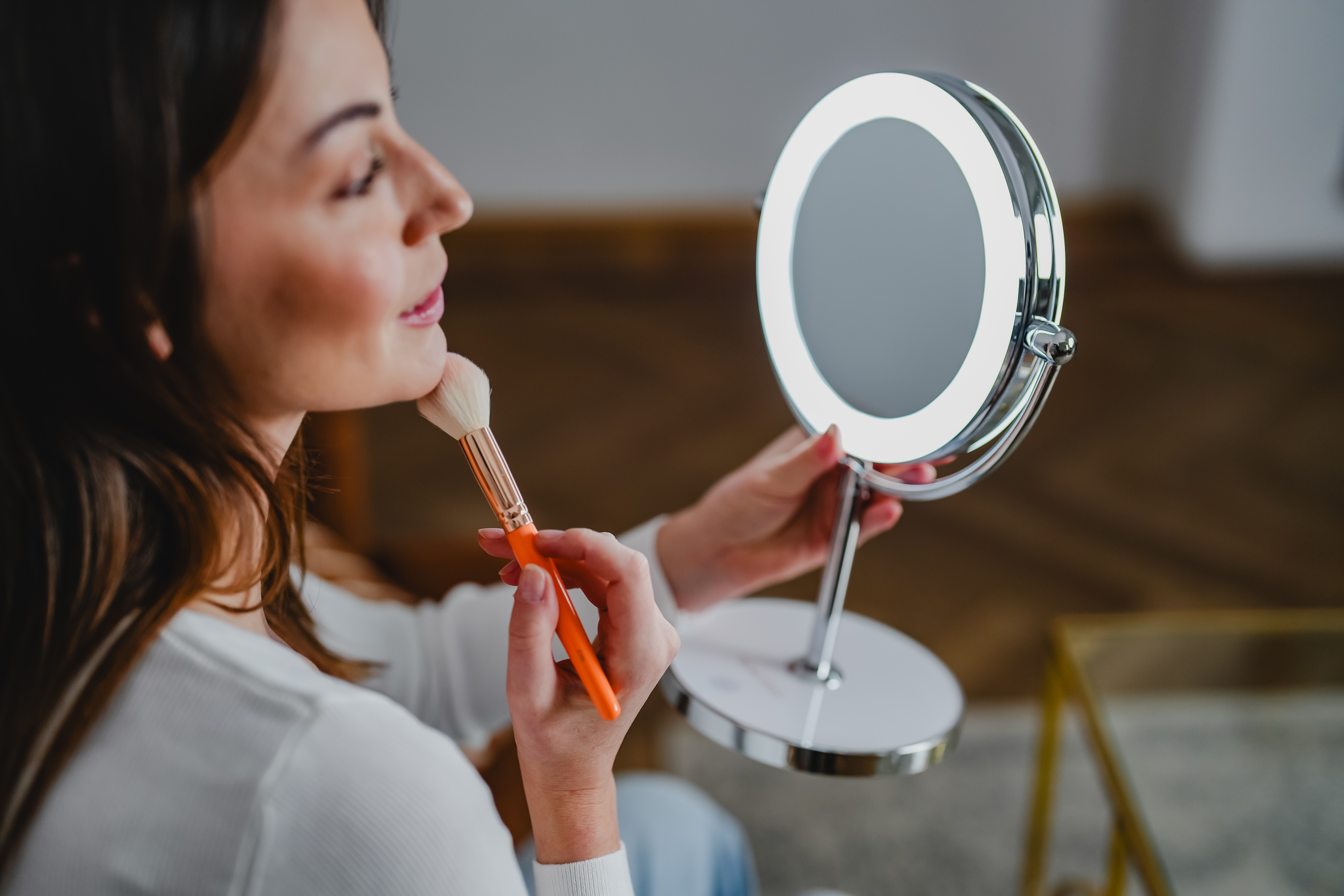 Frau mit Make-up-Pinsel und beleuchtetem Spiegel