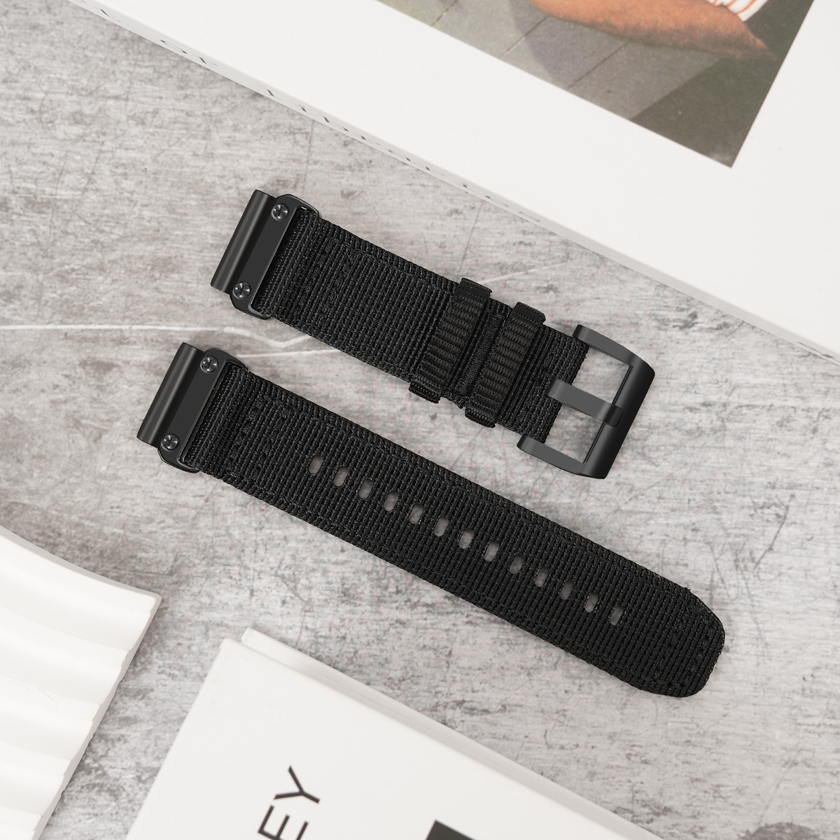 Zwei schwarze Stoffuhrenarmbänder mit schwarzen Metallschnallen liegen auf einem grauen Untergrund.