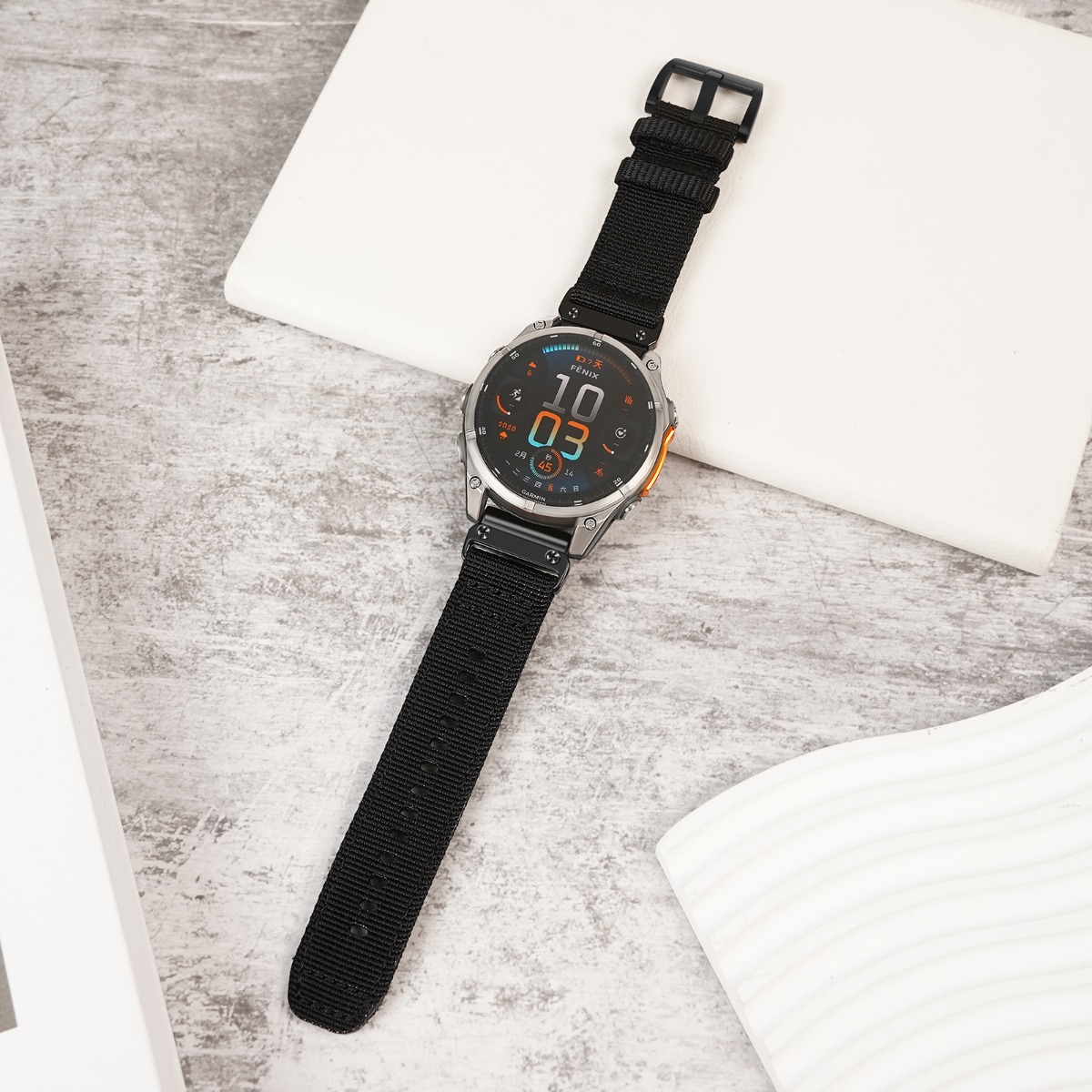 Silberne Smartwatch mit schwarzem Stoffarmband auf grauem Untergrund.