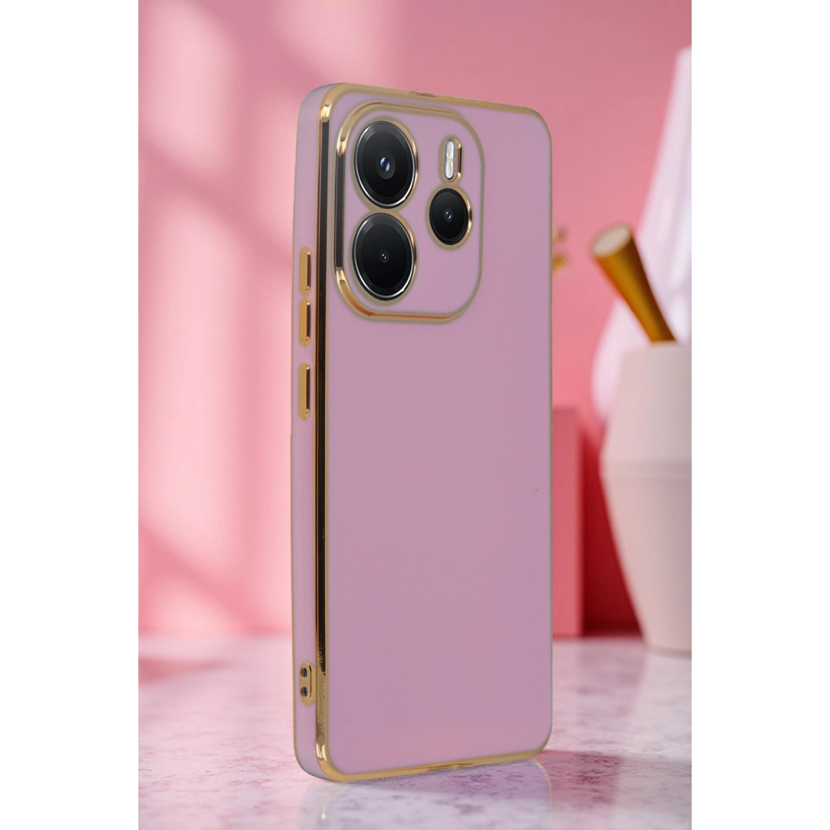 Altın kenarlıklı ve kamera çerçeveli açık pembe telefon kılıfı.