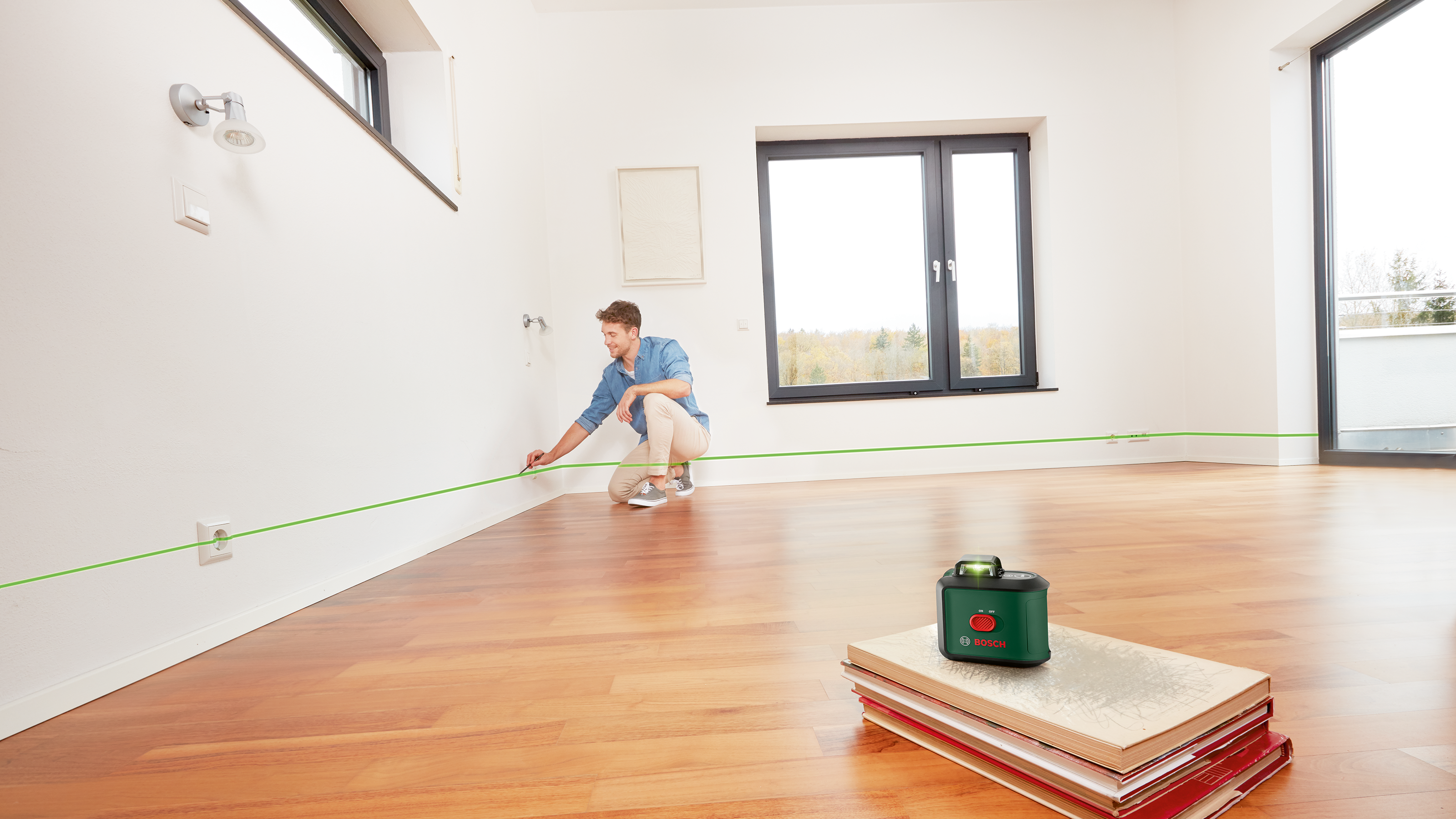 Mężczyzna rysuje linię na ścianie zielonym laserem w pustym pokoju.