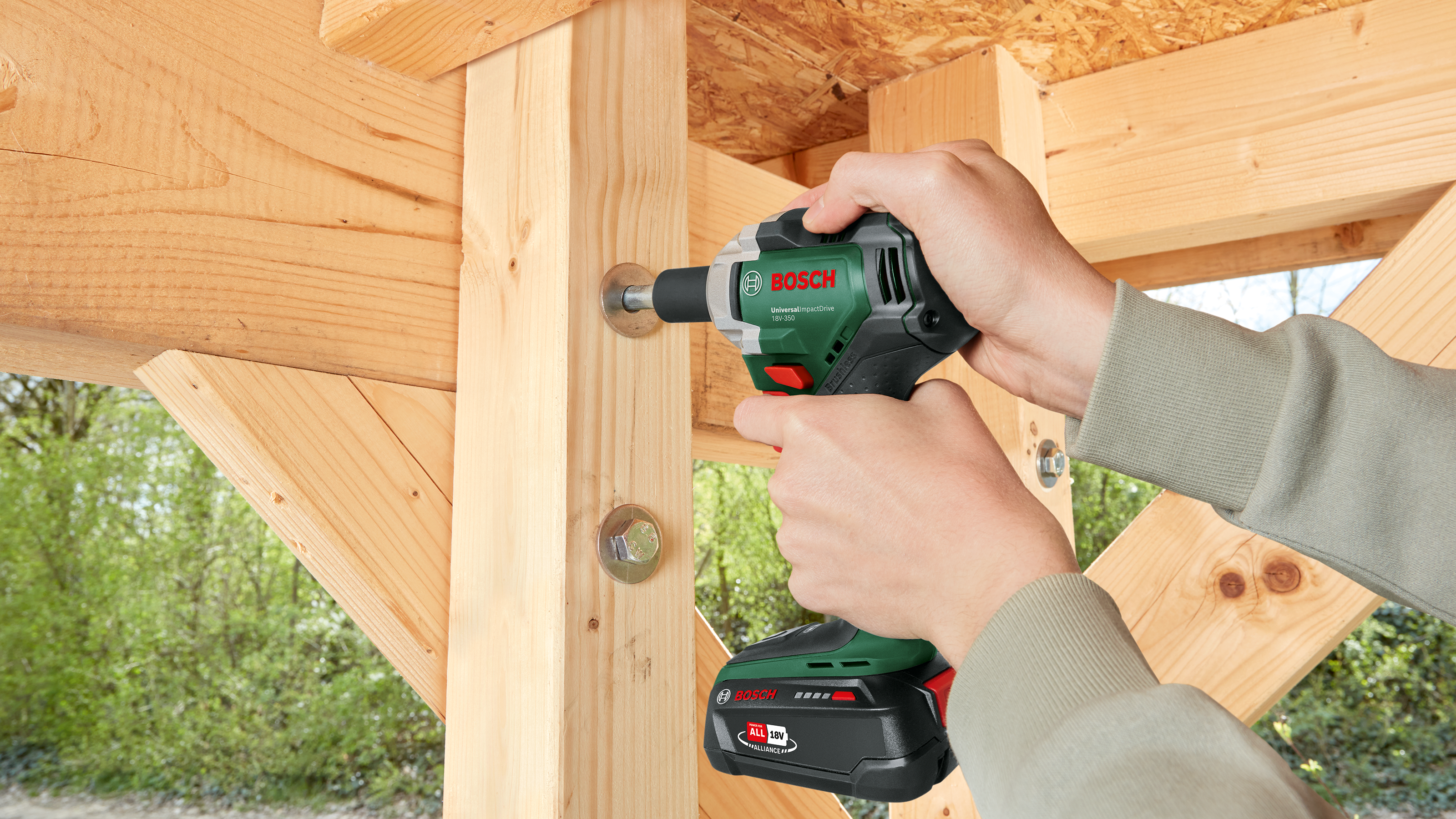 Eine Person benutzt einen grünen Bosch Akkuschrauber, um eine Schraube in Holz zu drehen.