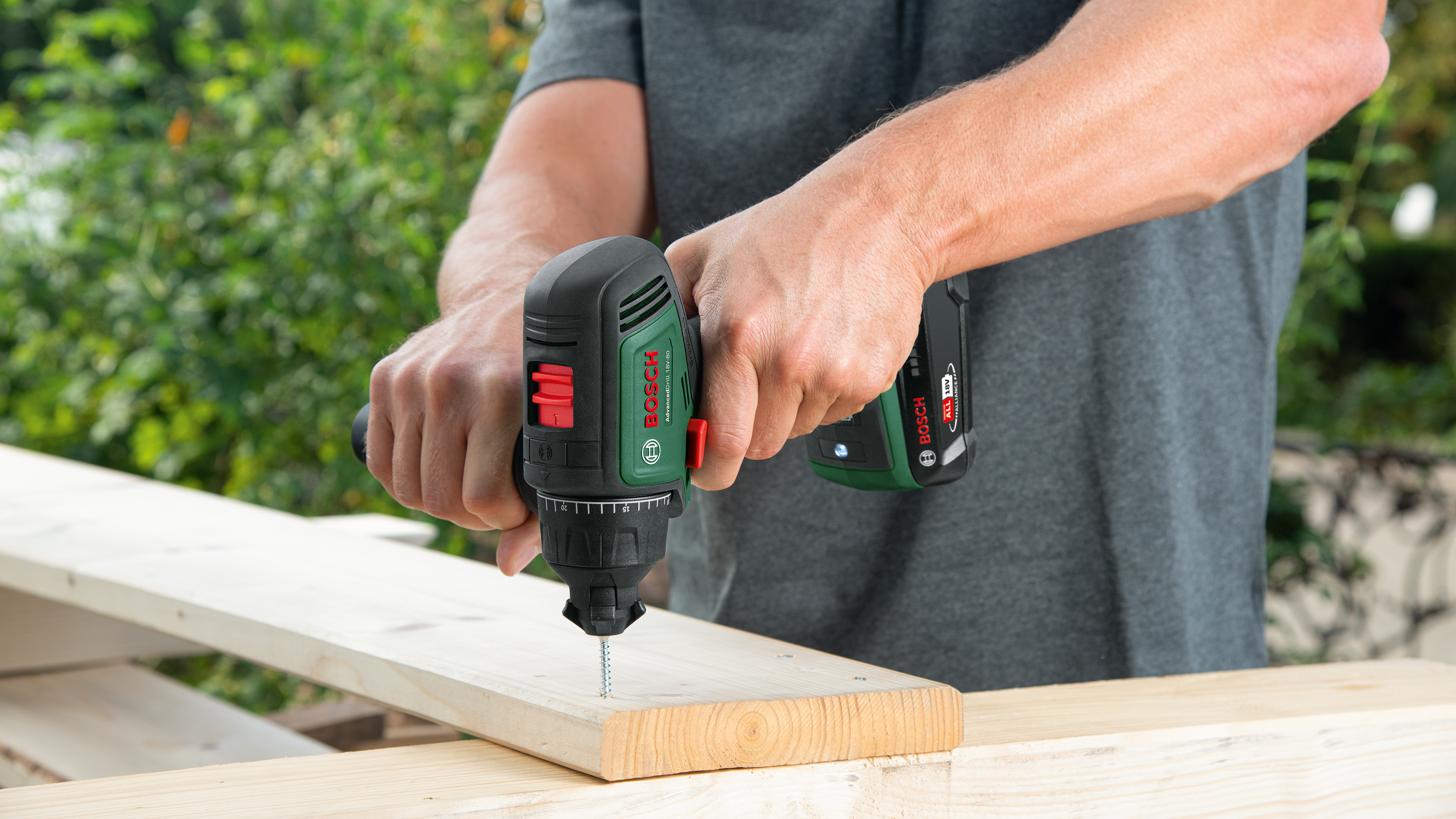 Ein Mann benutzt einen grünen Bosch Akkuschrauber, um eine Schraube in Holz zu drehen.