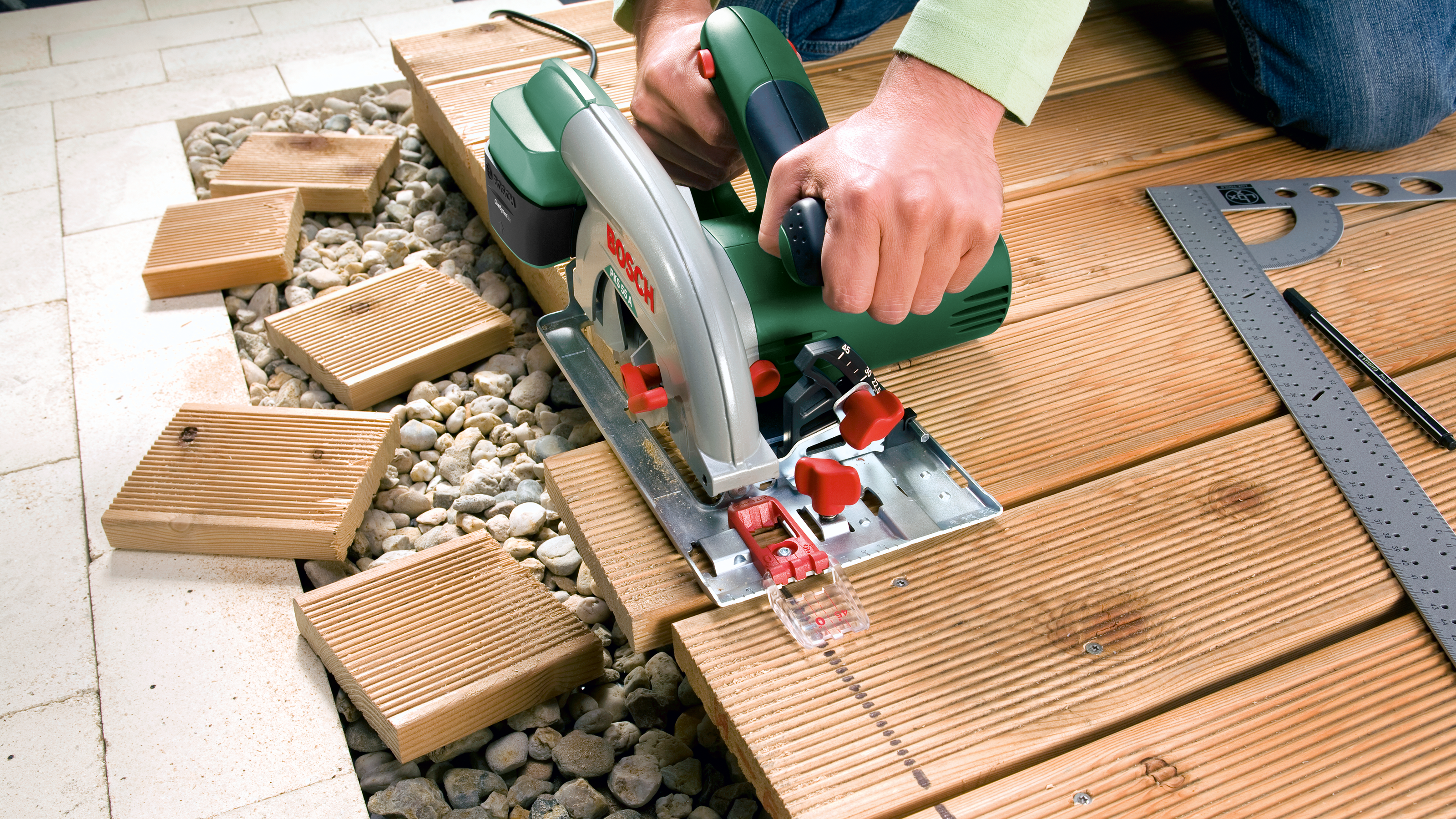 Ein Mann schneidet mit einer Kreissäge Holzbretter für eine Terrasse zu.