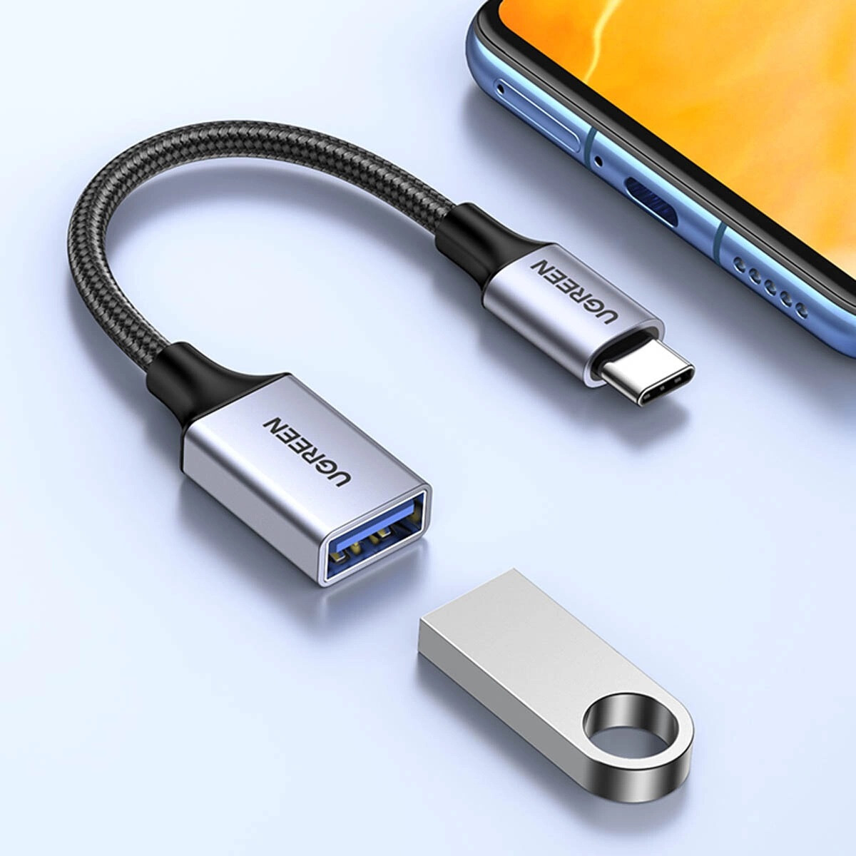 Adapter USB-C na USB-A leży obok pendrive'a i telefonu komórkowego.