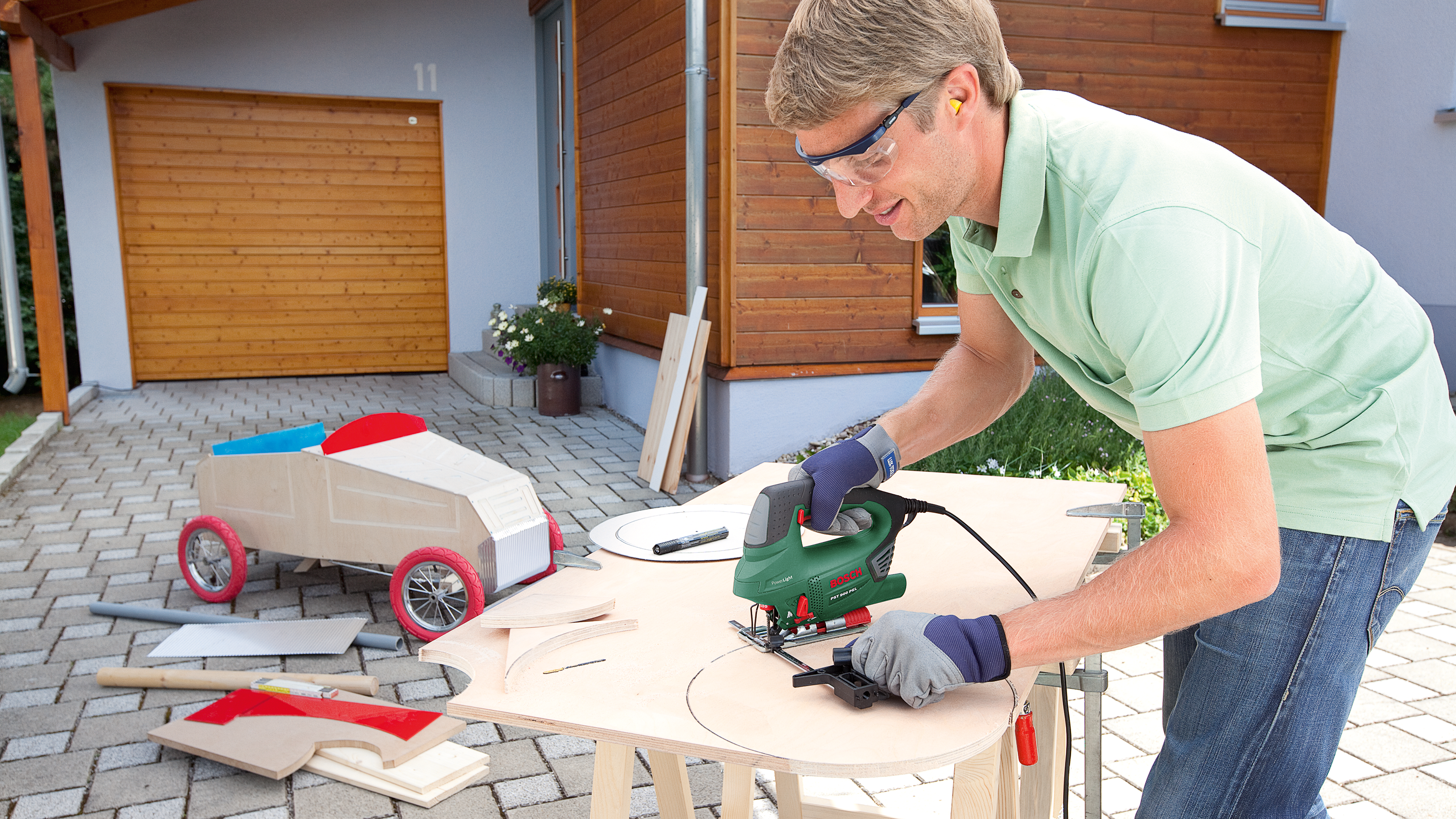 Mężczyzna pracuje przy drewnie piłą, budowa samochodu w tle.