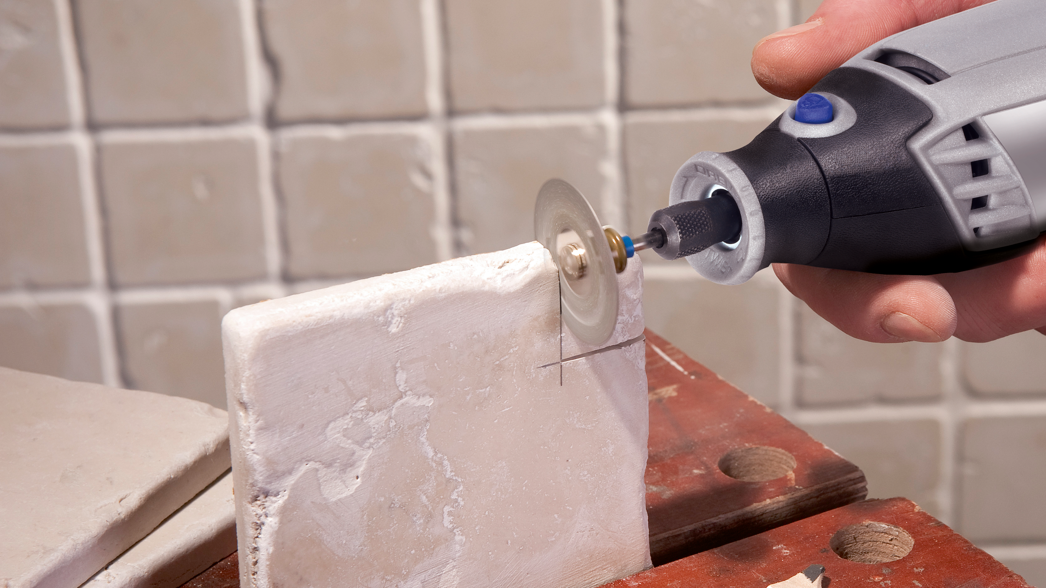 Een persoon gebruikt een Dremel-gereedschap met een snijwiel om een wit object te snijden.