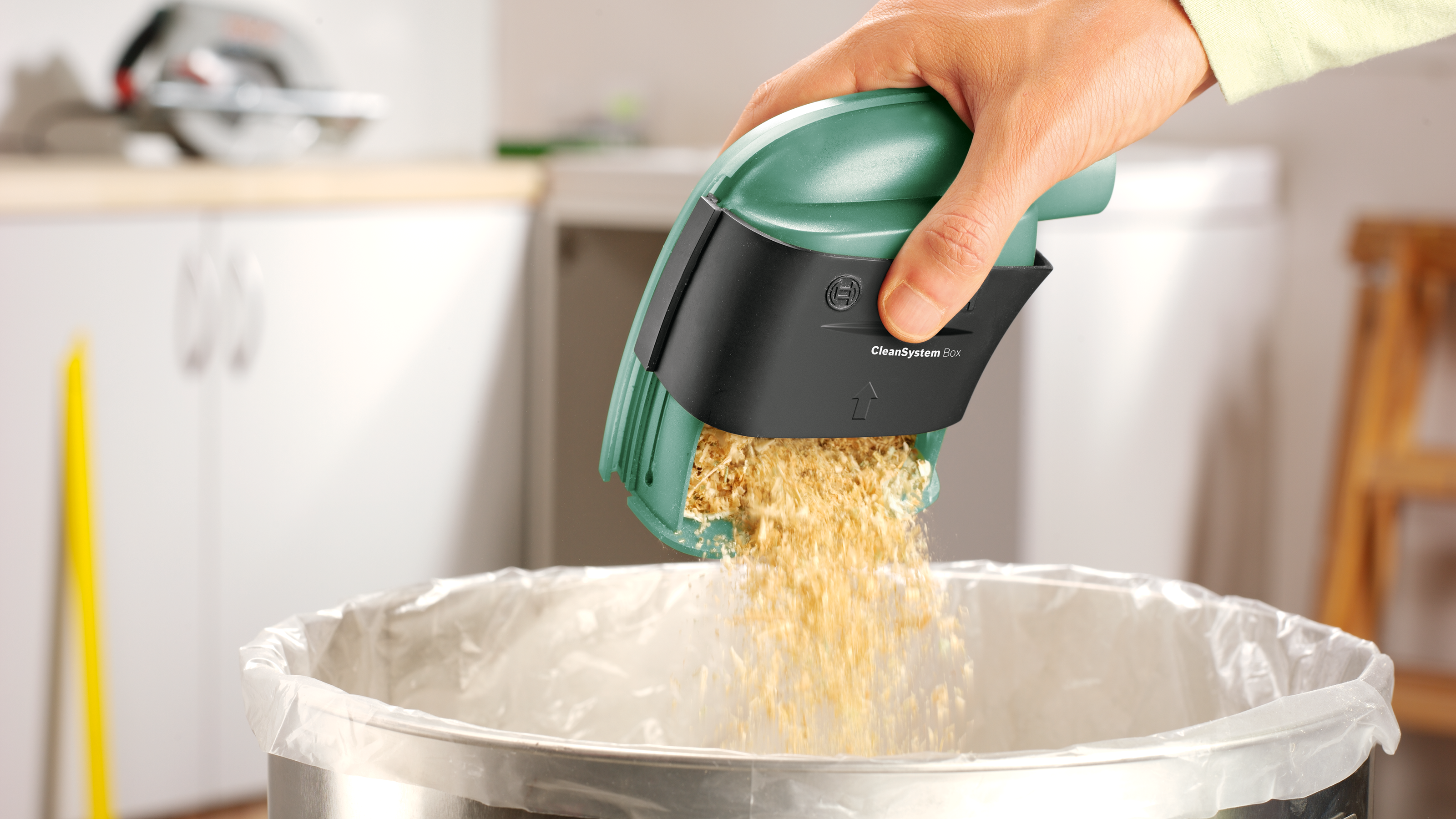 Zielony pojemnik z trocinami jest opróżniany do kosza na śmieci.