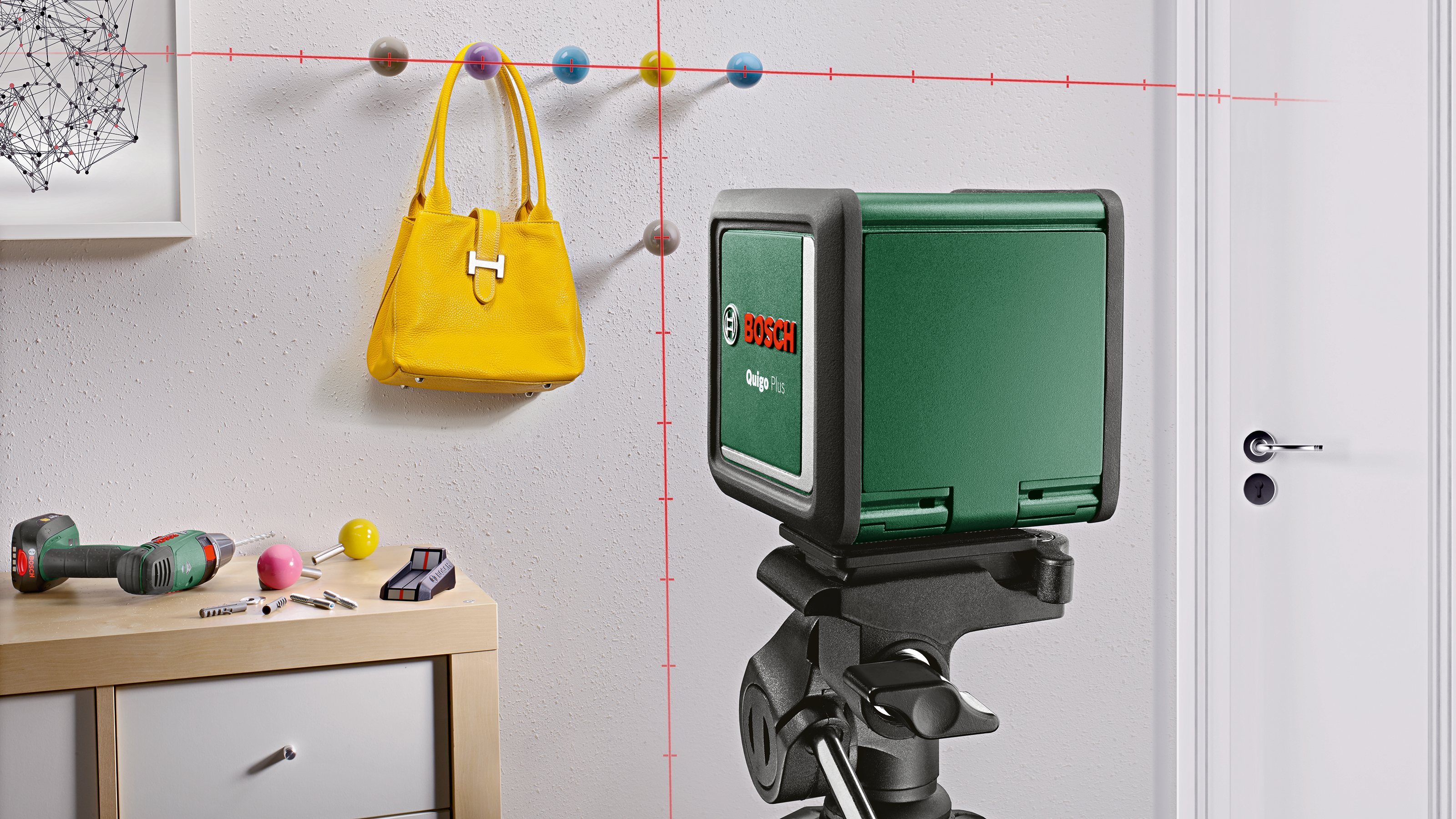 Zielony laserowy poziomica na statywie, obok wiertarki i żółtej torby.